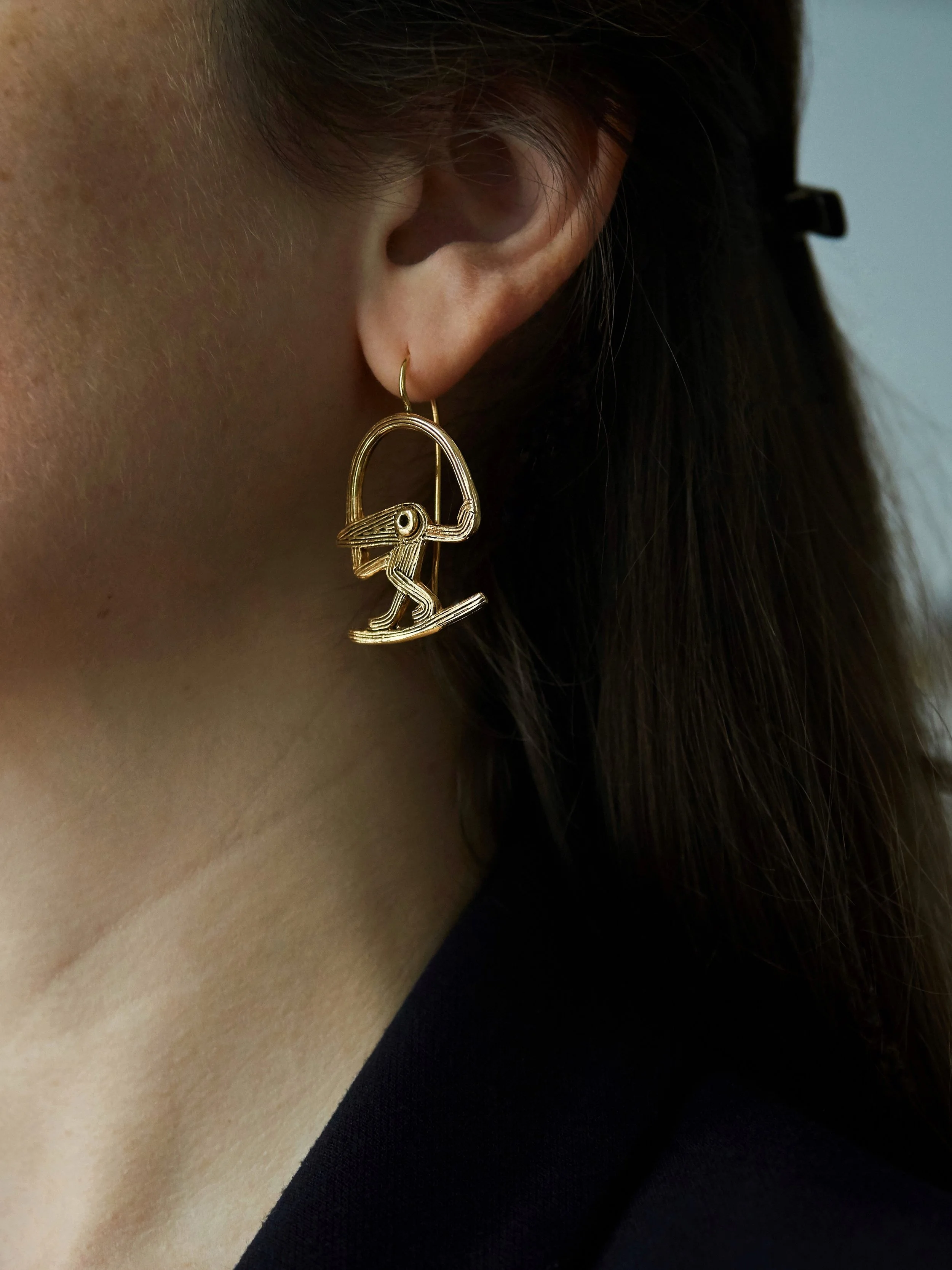 Close-up of Cordeli bird earrings in gold-plated bronze by Elisabeth Riveiro, sculptural handcrafted jewellery, worn – AMBART Palma.