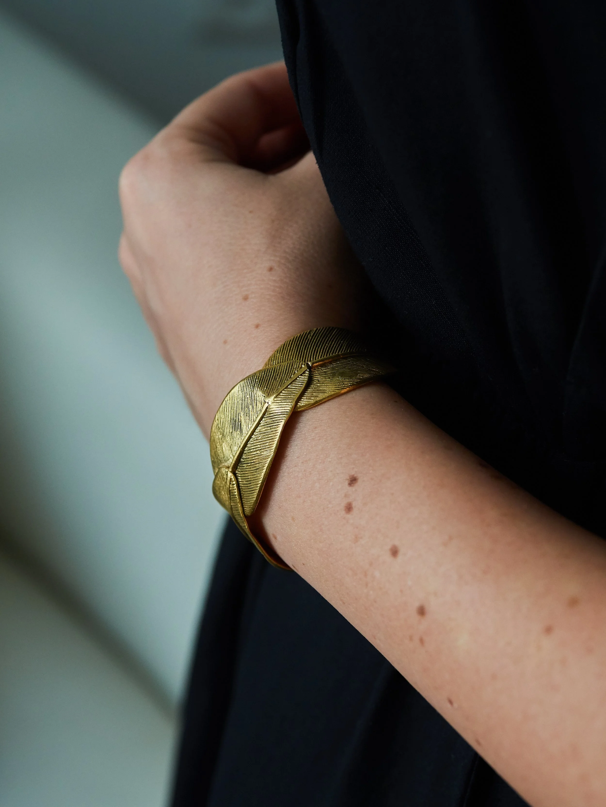 Detail of the Olympe gold-plated bronze cuff bracelet by Elisabeth Riveiro, featuring delicately engraved leaf motifs, overlapping organic forms and luminous golden surfaces.