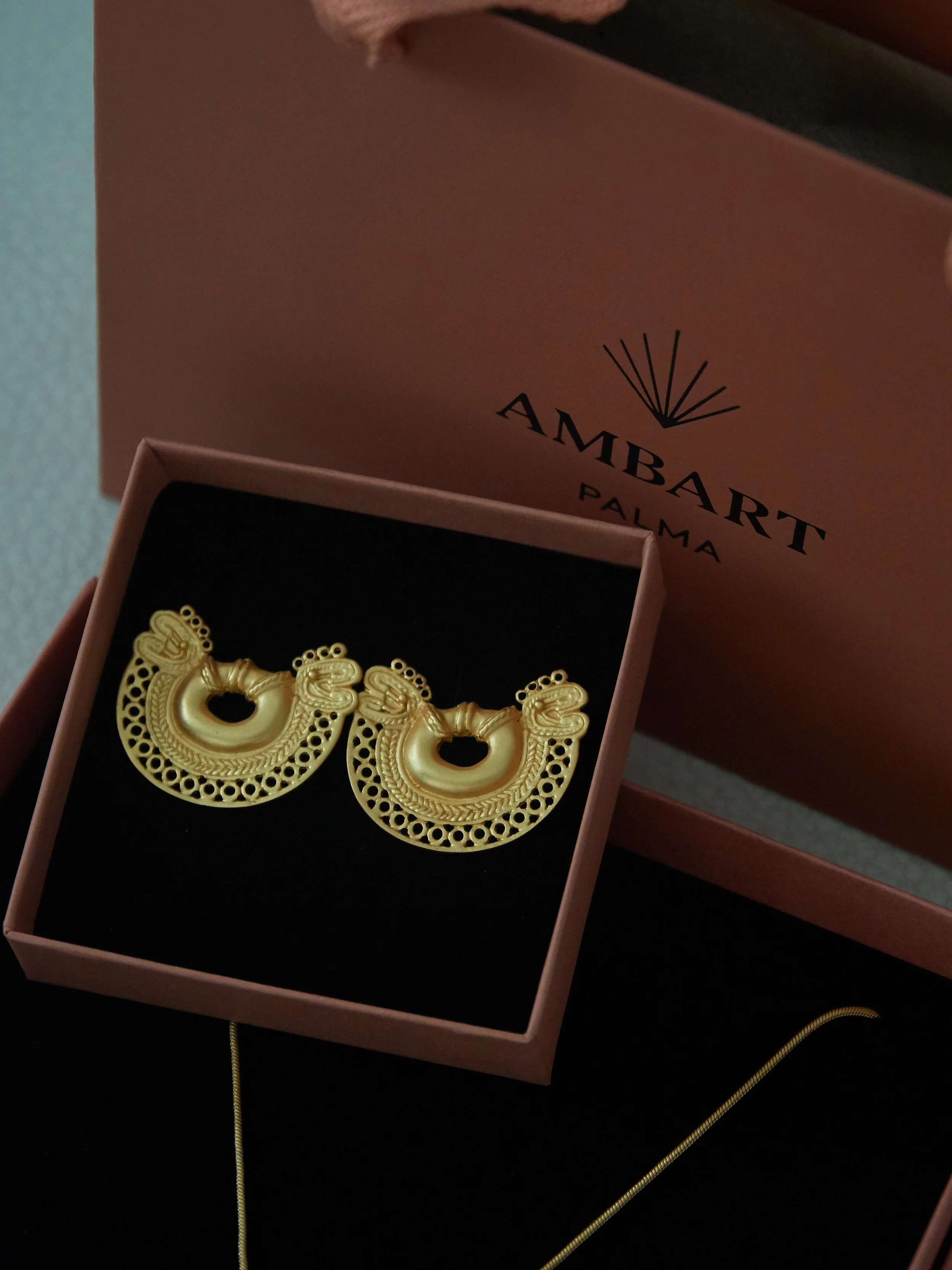 Pair of gold-plated Tairona-inspired double-headed serpent earrings displayed in an AMBART jewellery box.