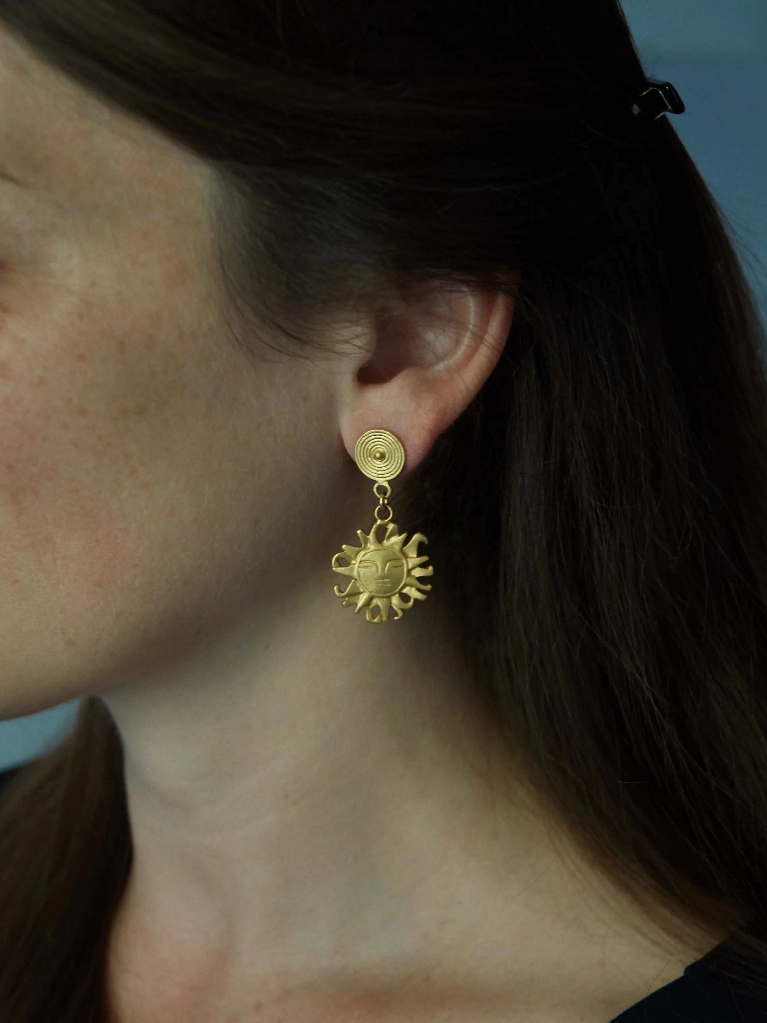 Gold-plated radiant face earrings from Galeria Eldorado, inspired by anthropomorphic imagery in pre-Columbian Colombian goldwork