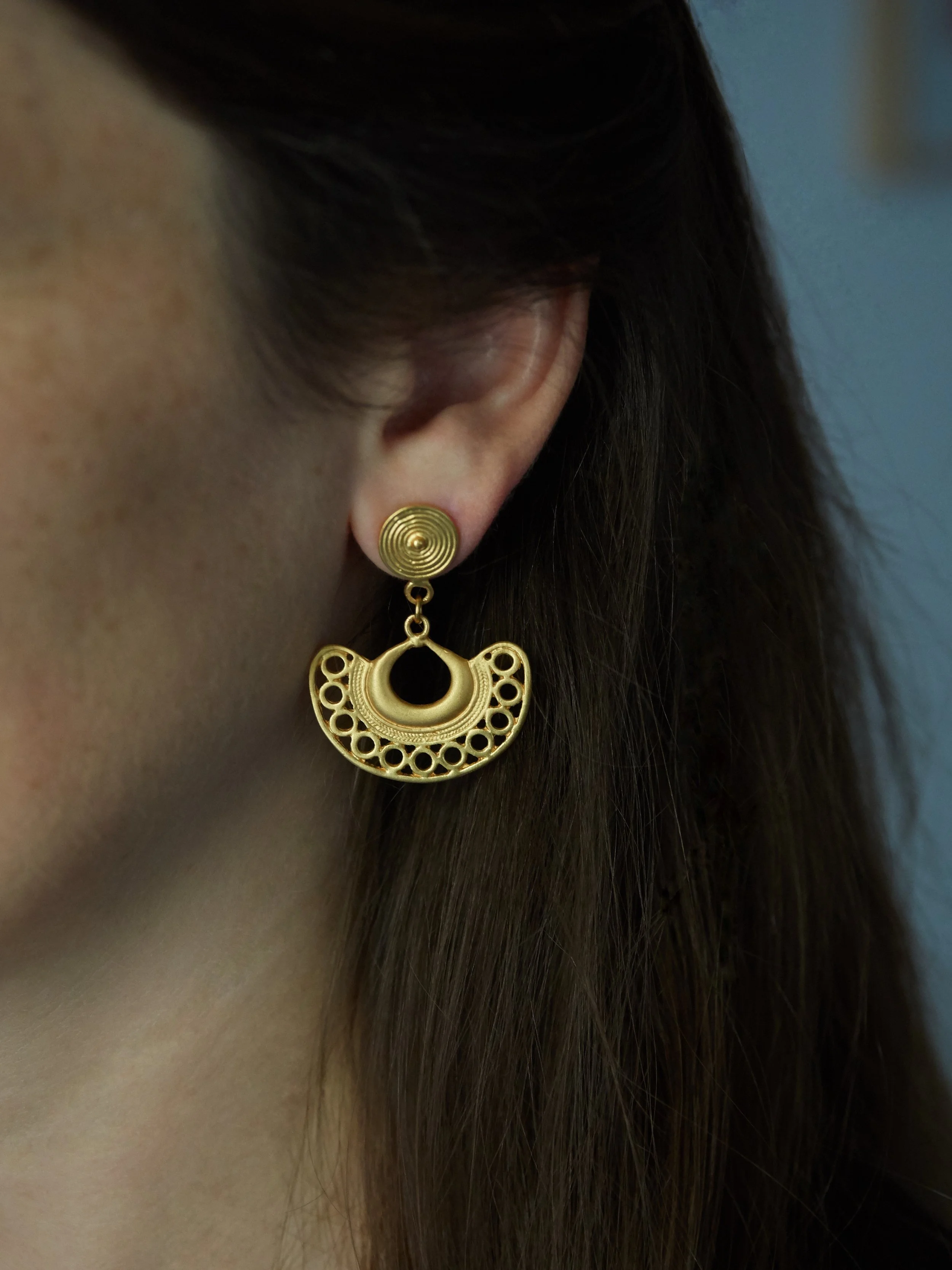 Close-up of gold-plated Tairona semilunar earrings worn on the ear, inspired by ancient pre-Columbian Colombian goldwork