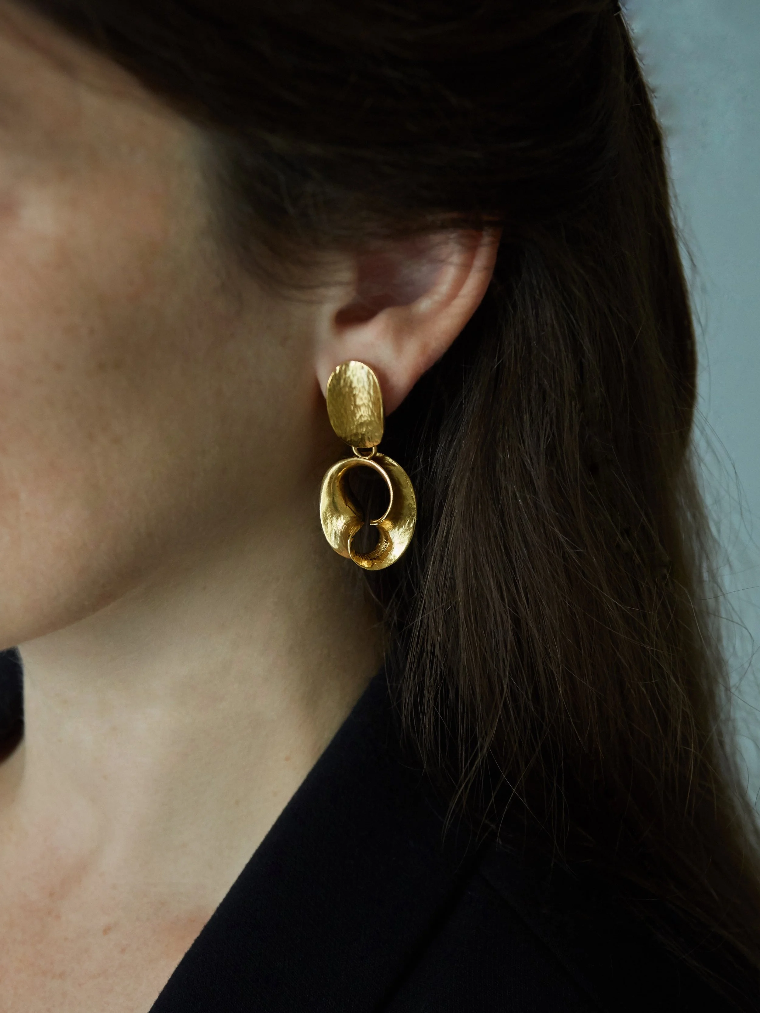 Elisabeth Riveiro’s Ovaljazz Small sculptural drop earrings in gold-plated bronze, featuring textured oval studs and openwork curved pendants, shown worn on the ear.