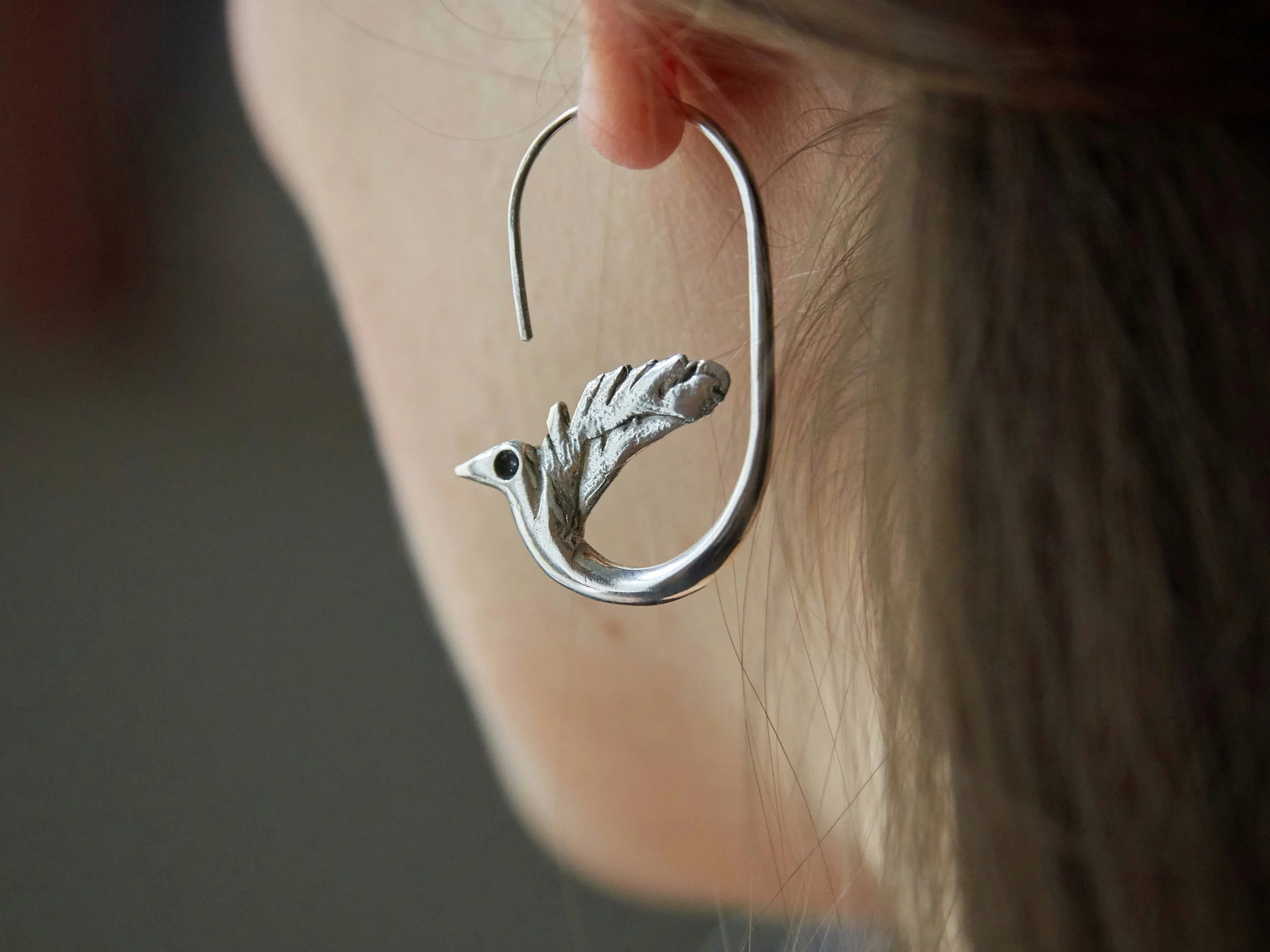 Silver-plated bronze bird earrings by Elisabeth Riveiro worn on ear, sculptural curved hook design
