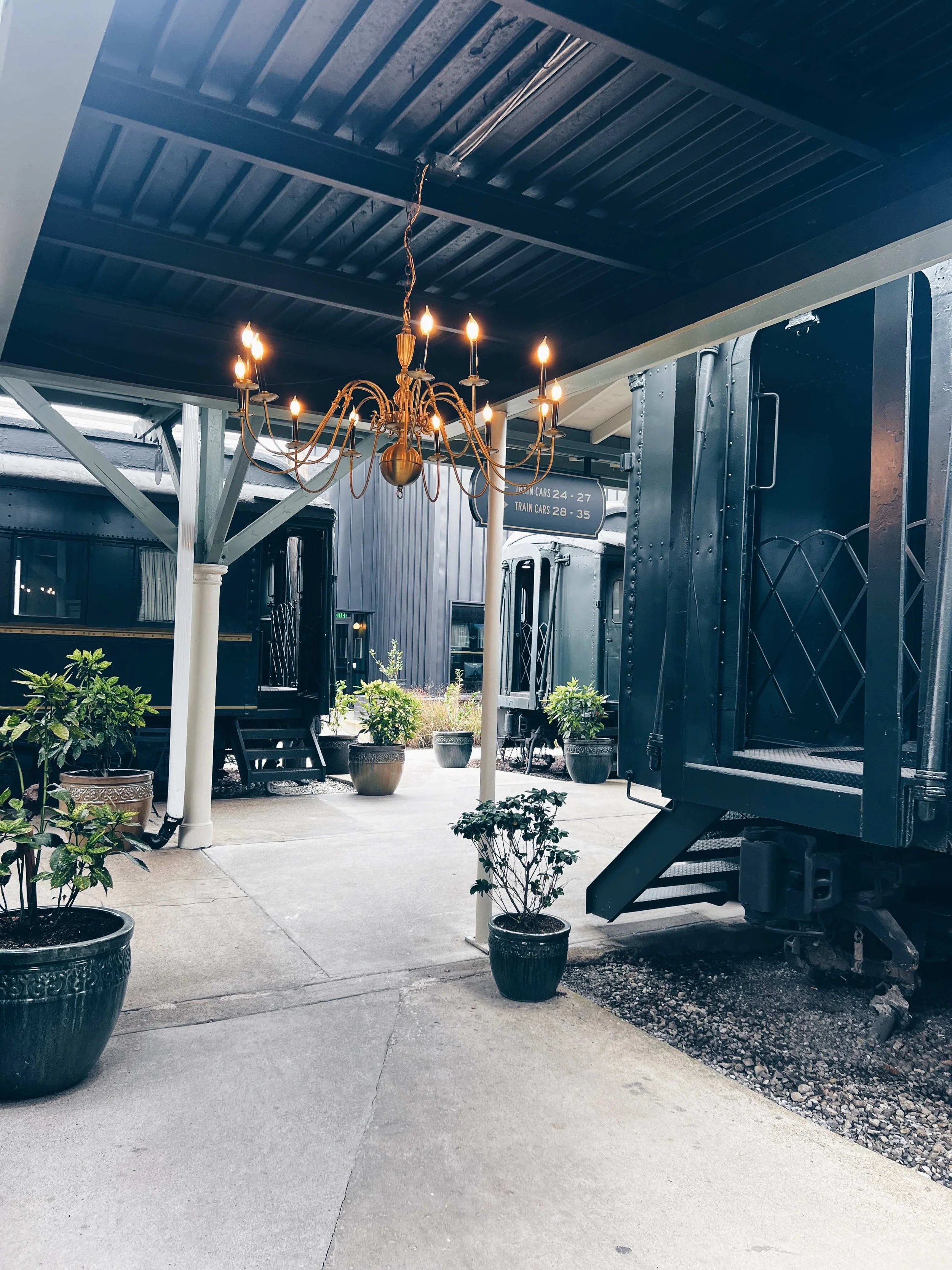 Outdoor walk ways of The Choo Choo Train hotel. A chandelier hangs in the walkway, and train car rooms are seen.