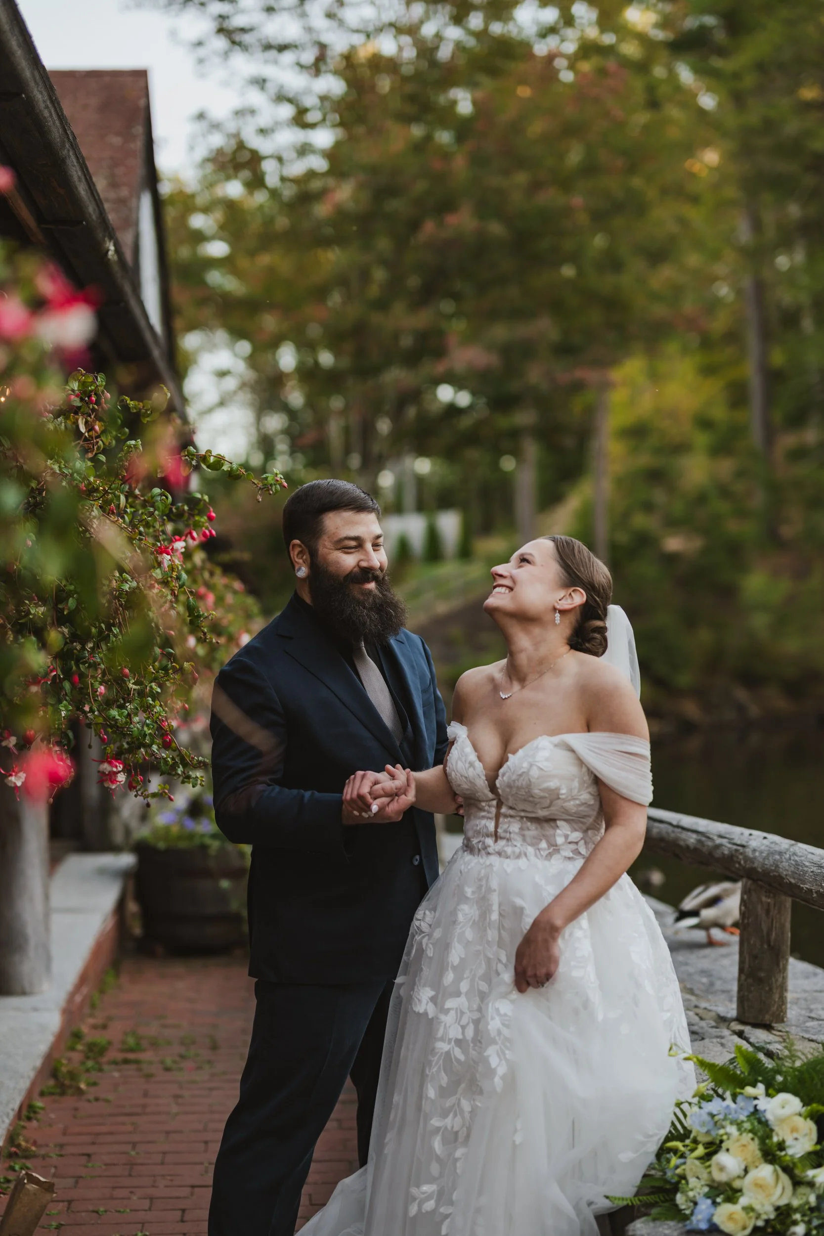 A newlywed couple holding hands as they stand next to a lake and laugh