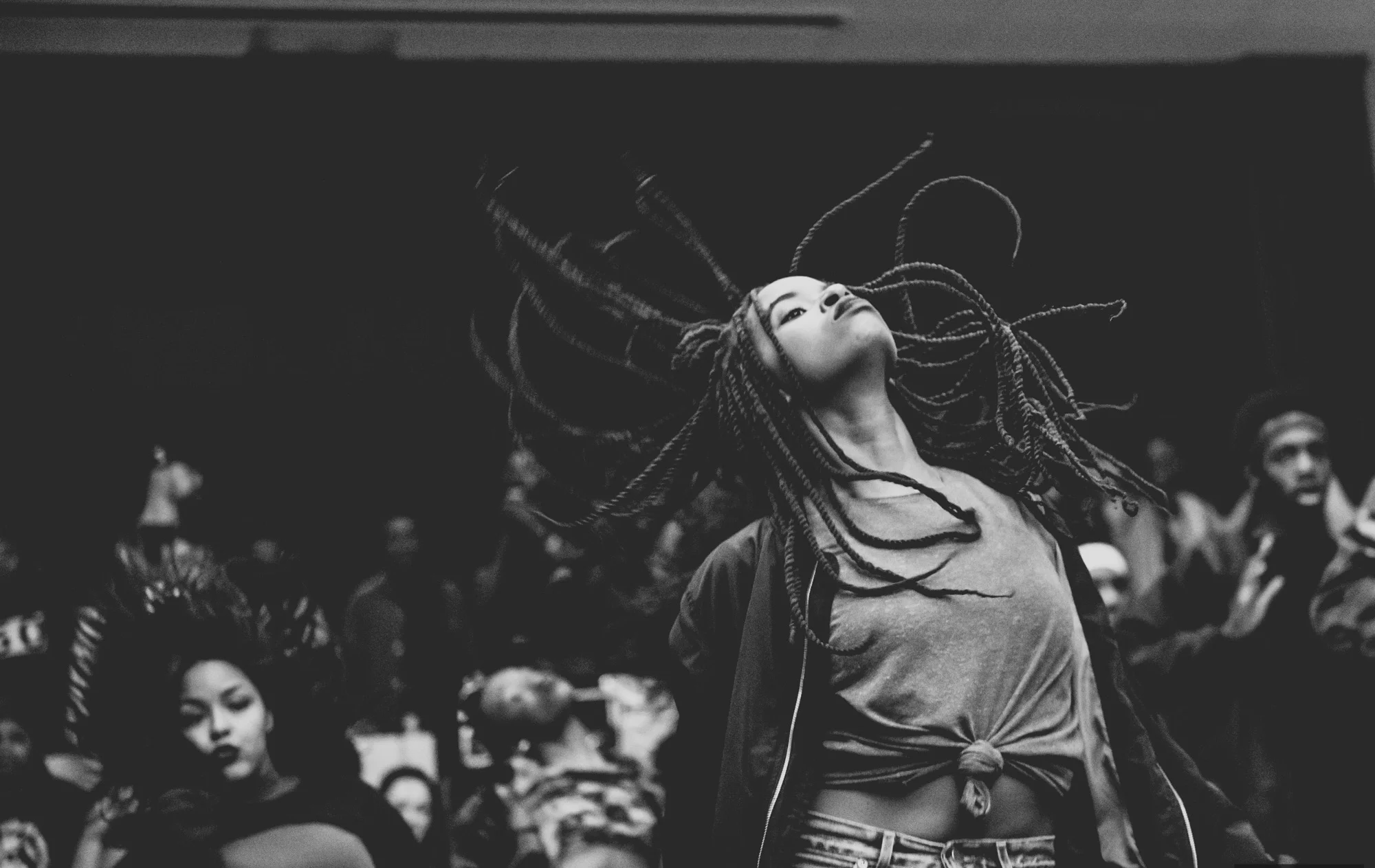 A breakdancer flips her hair mid-move with backup dancers dancing behind her.