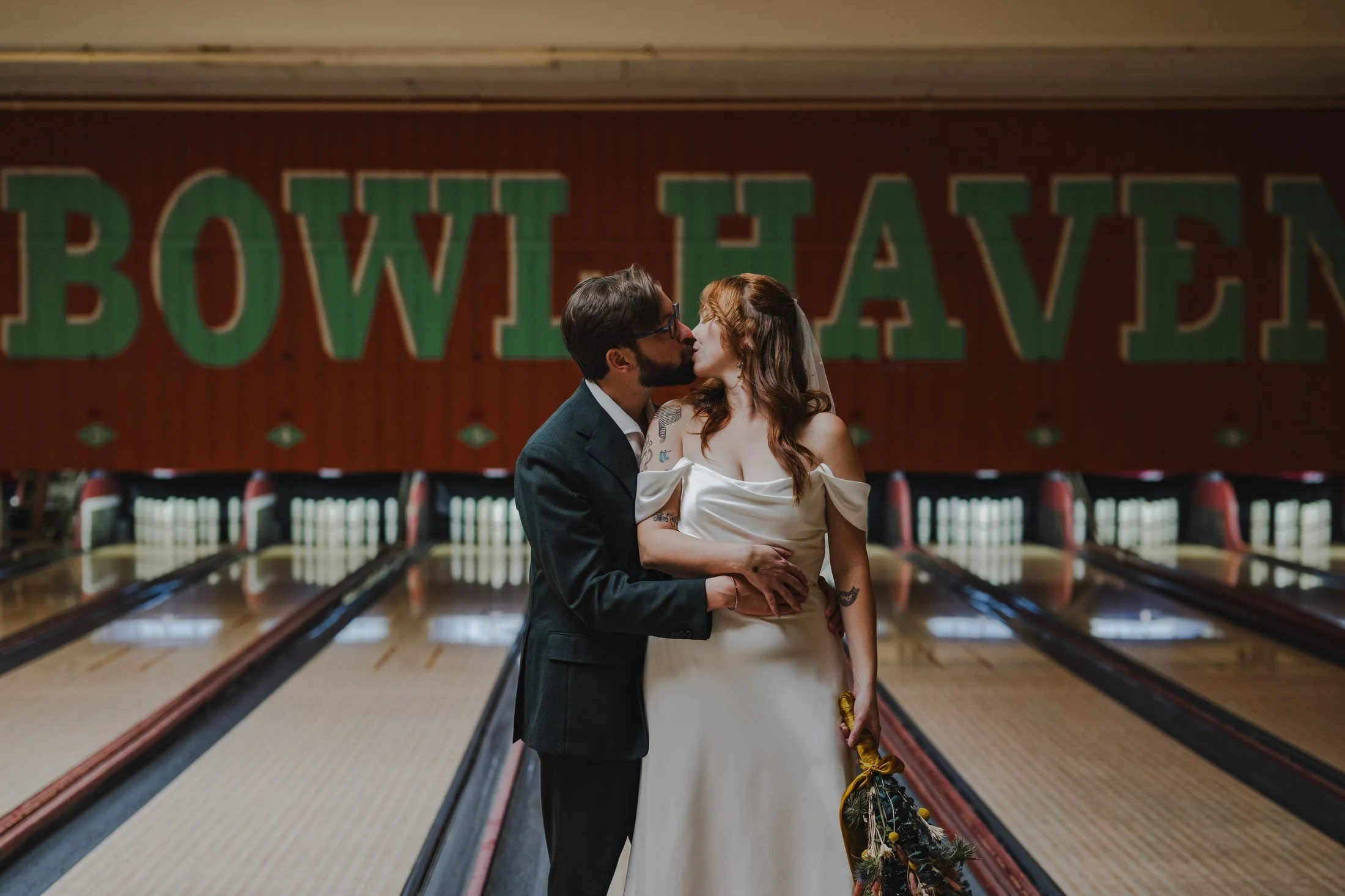 A newlywed couple kissing as they stand in a bowling alley