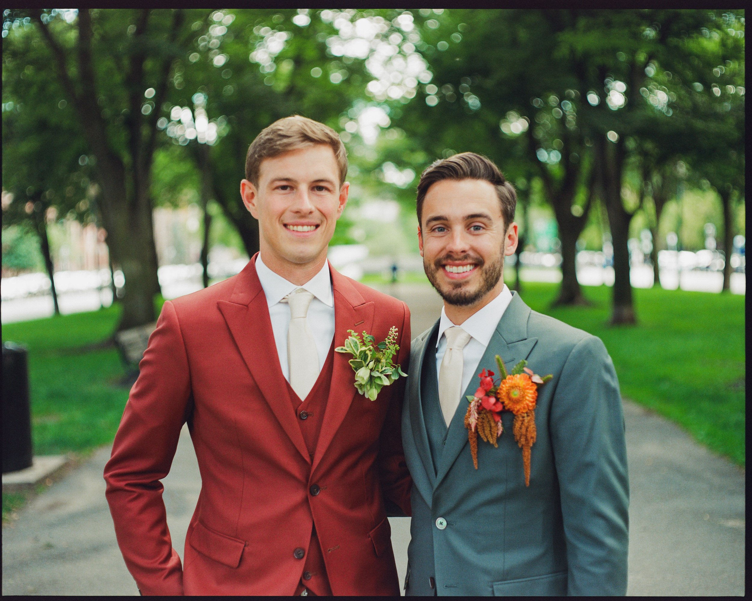 A newlywed couple in suits smiling with their arms around each other