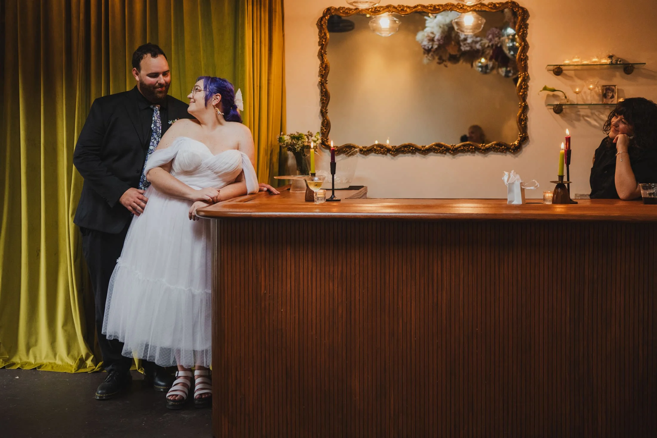 A newlywed couple standing by a bar as they smile at each other