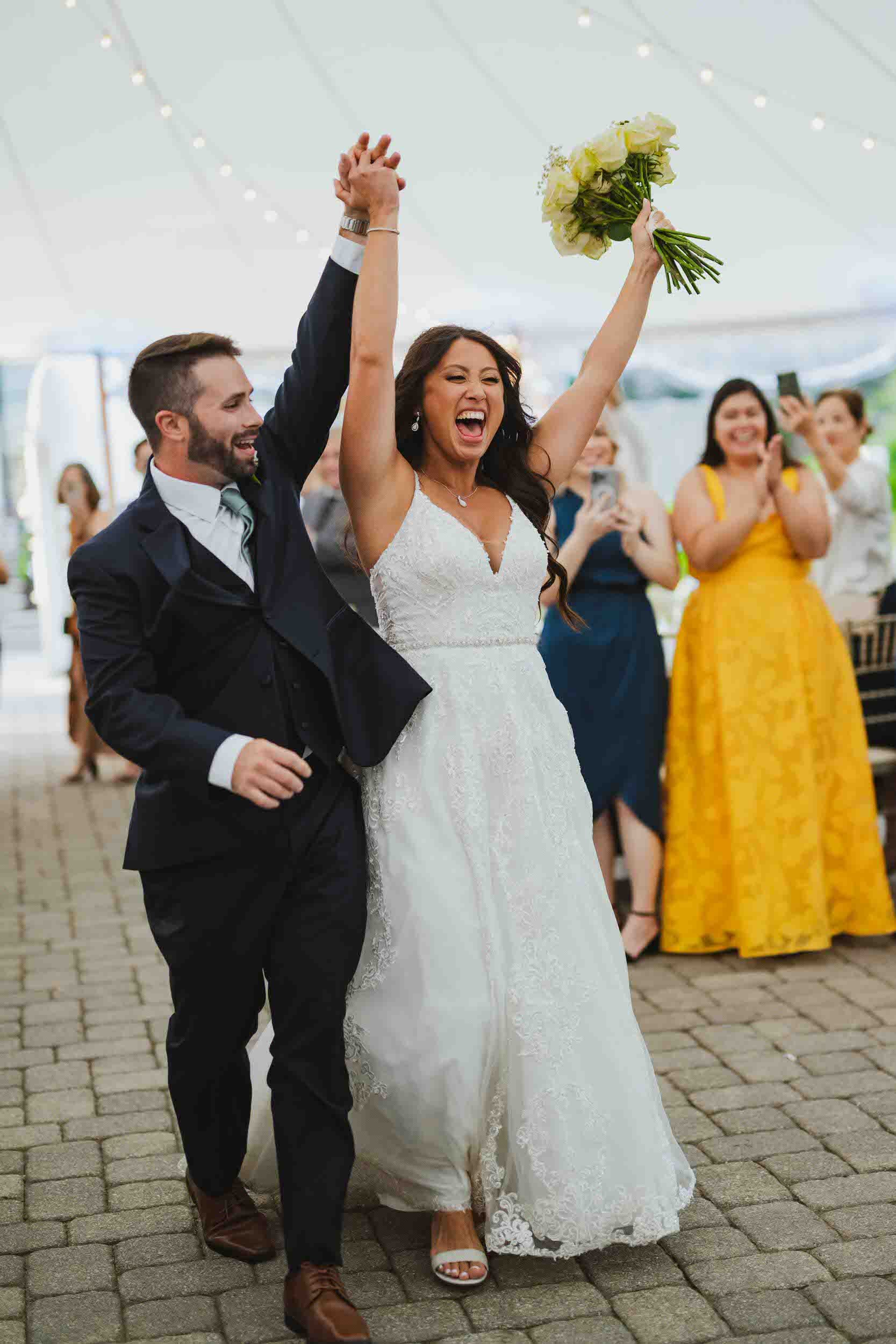 A newlywed couple holding their hands up celebrating as they walk into their reception