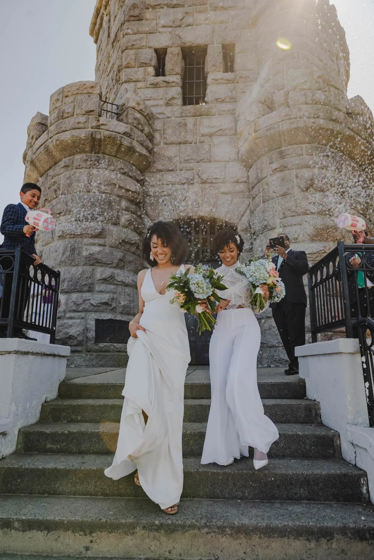 A newlywed couple walking down a staircase together as guests blow bubbles around them