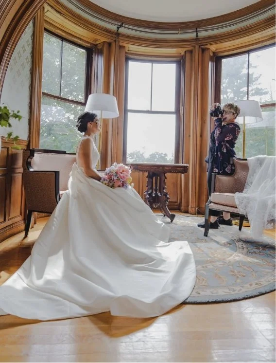 Amanda photographing a newlywed in a wedding dress sitting on a chair
