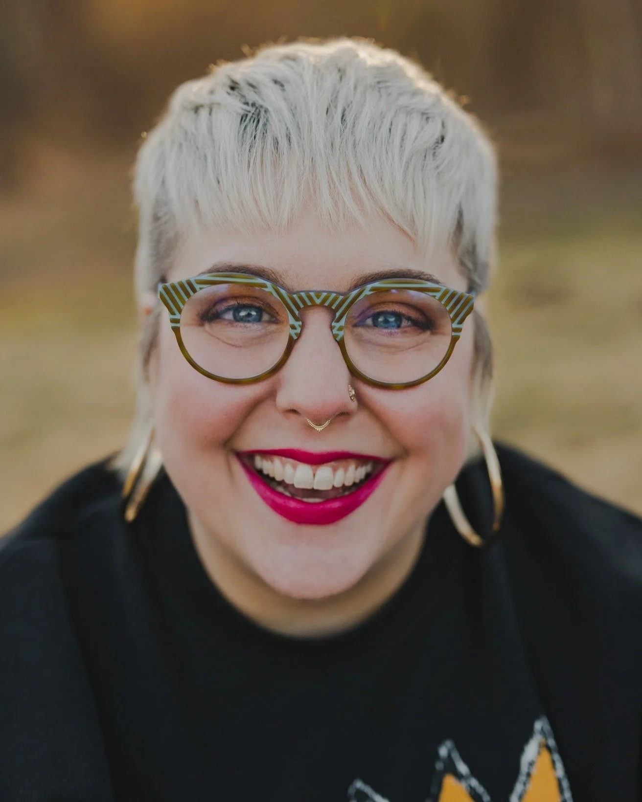A happy blonde girl with blue frames and hoop earrings smiles at the camera.