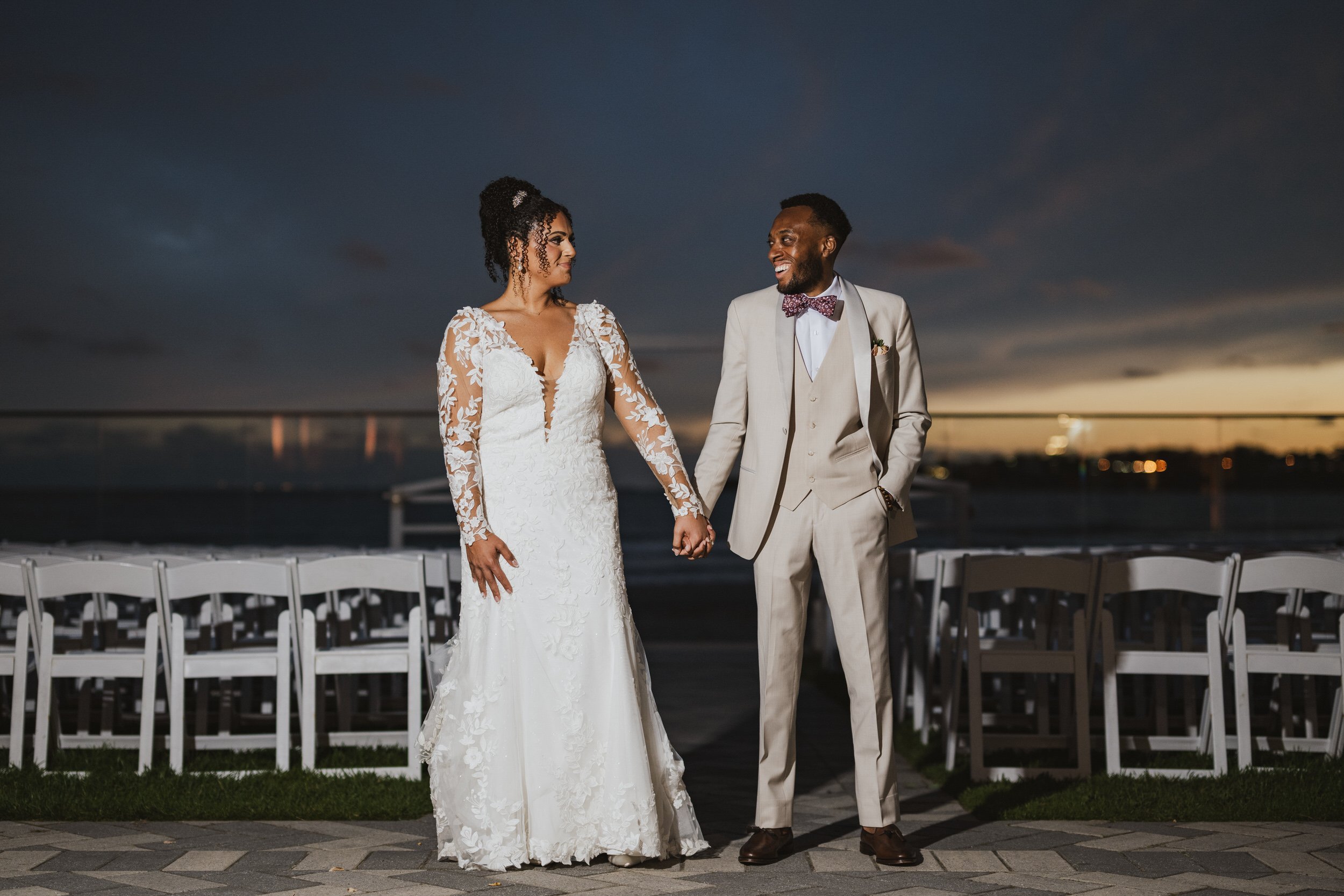A newlywed couple holding hands as they stand on a dock