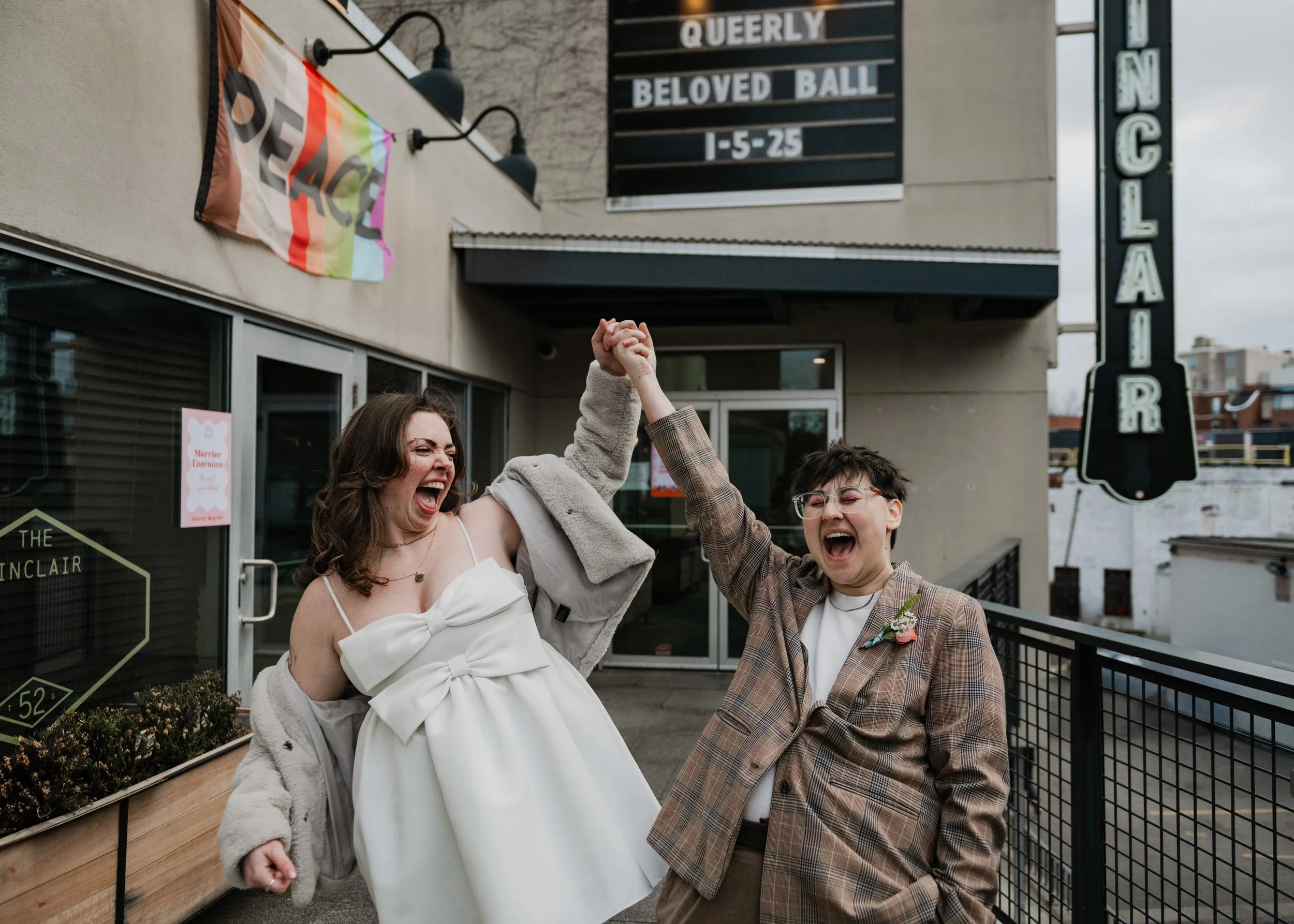 A newlywed couple raises their hands in the air outside of their wedding venue as they scream with joy.