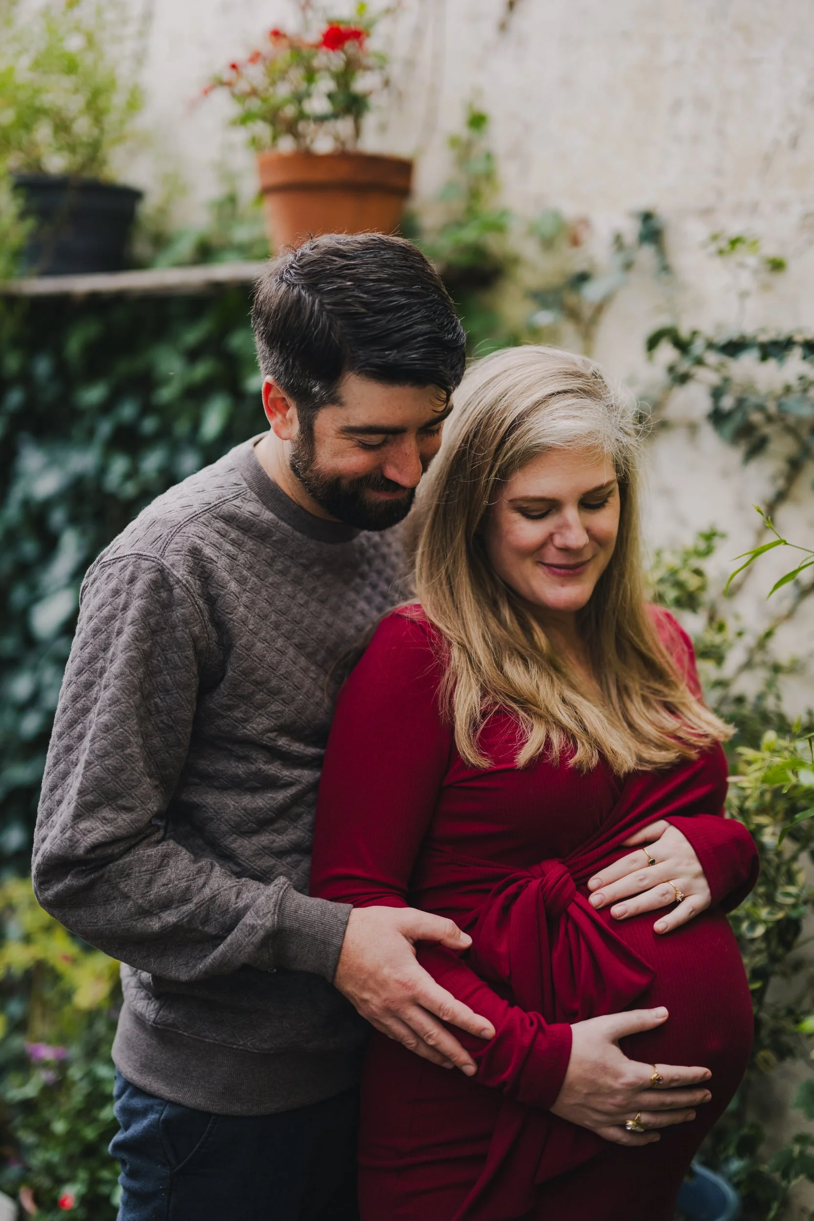 A pregnant couple standing one in front of the other while one holds their stomach