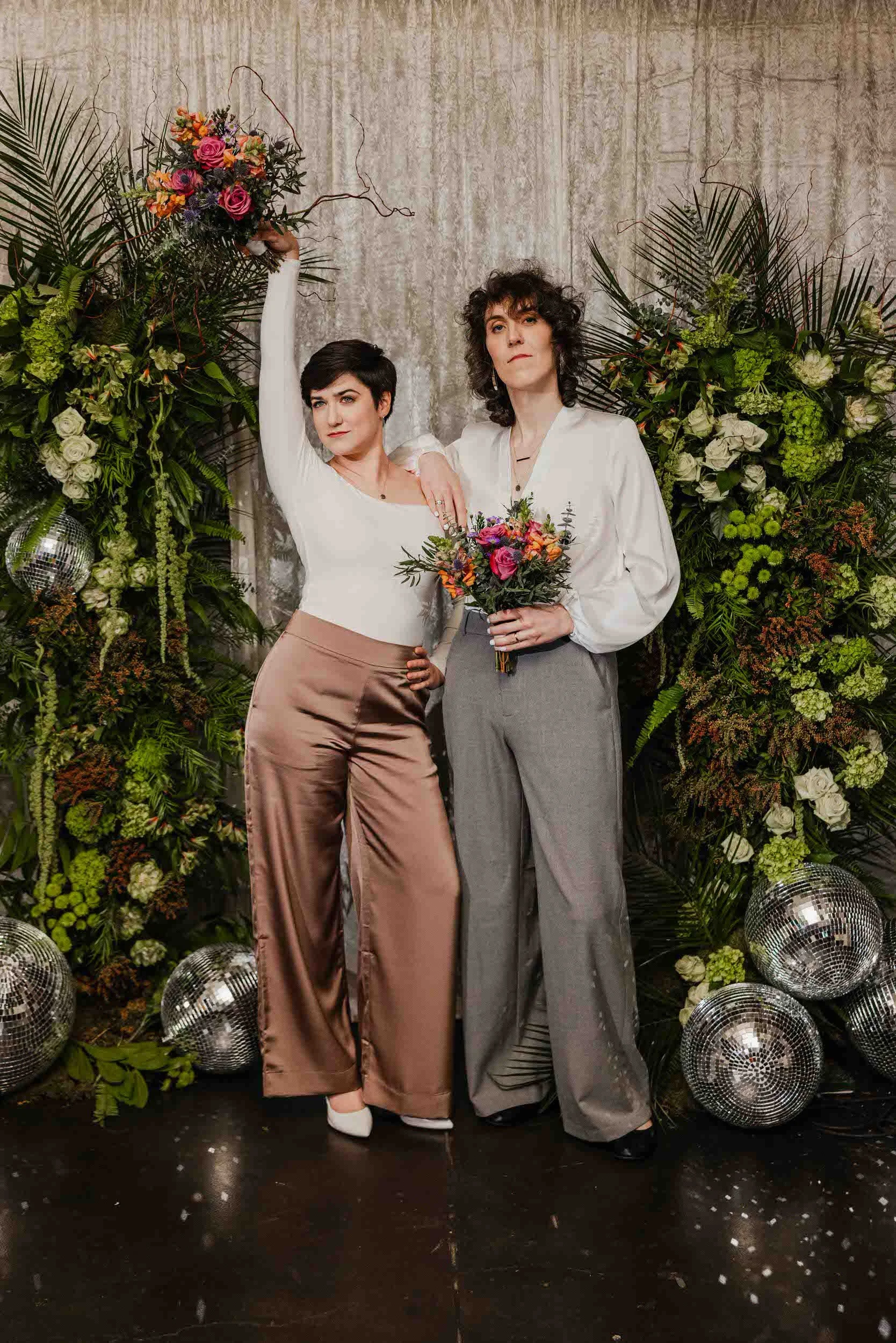 A newlywed couple posing together as they both hold bouquets of flowers
