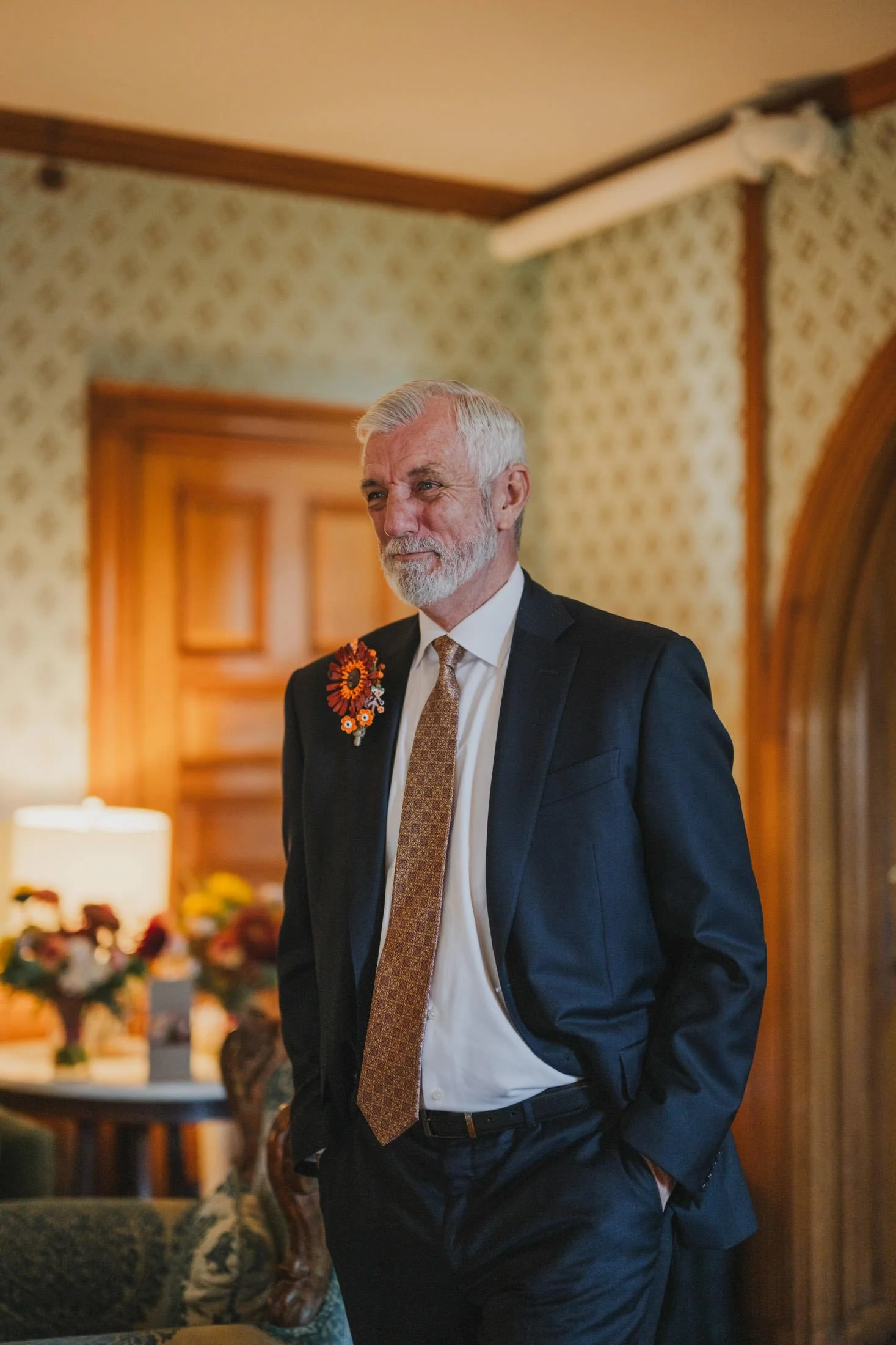 A person in a suit with their hands in their pocket as they smile and tear up