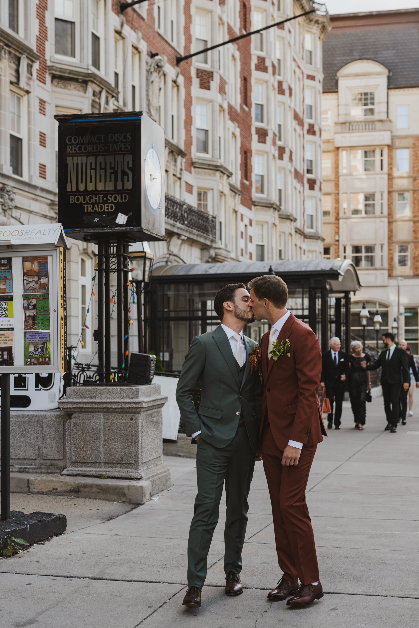 A newlywed couple kissing while they stand on a city sidewalk