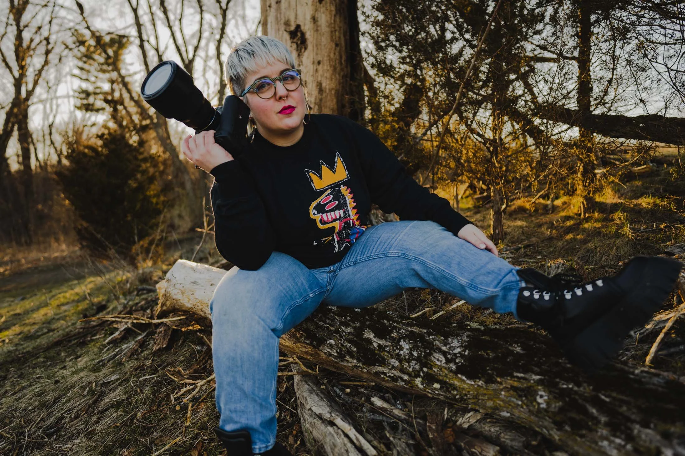 Amanda sitting on a log holding a camera up with one hand
