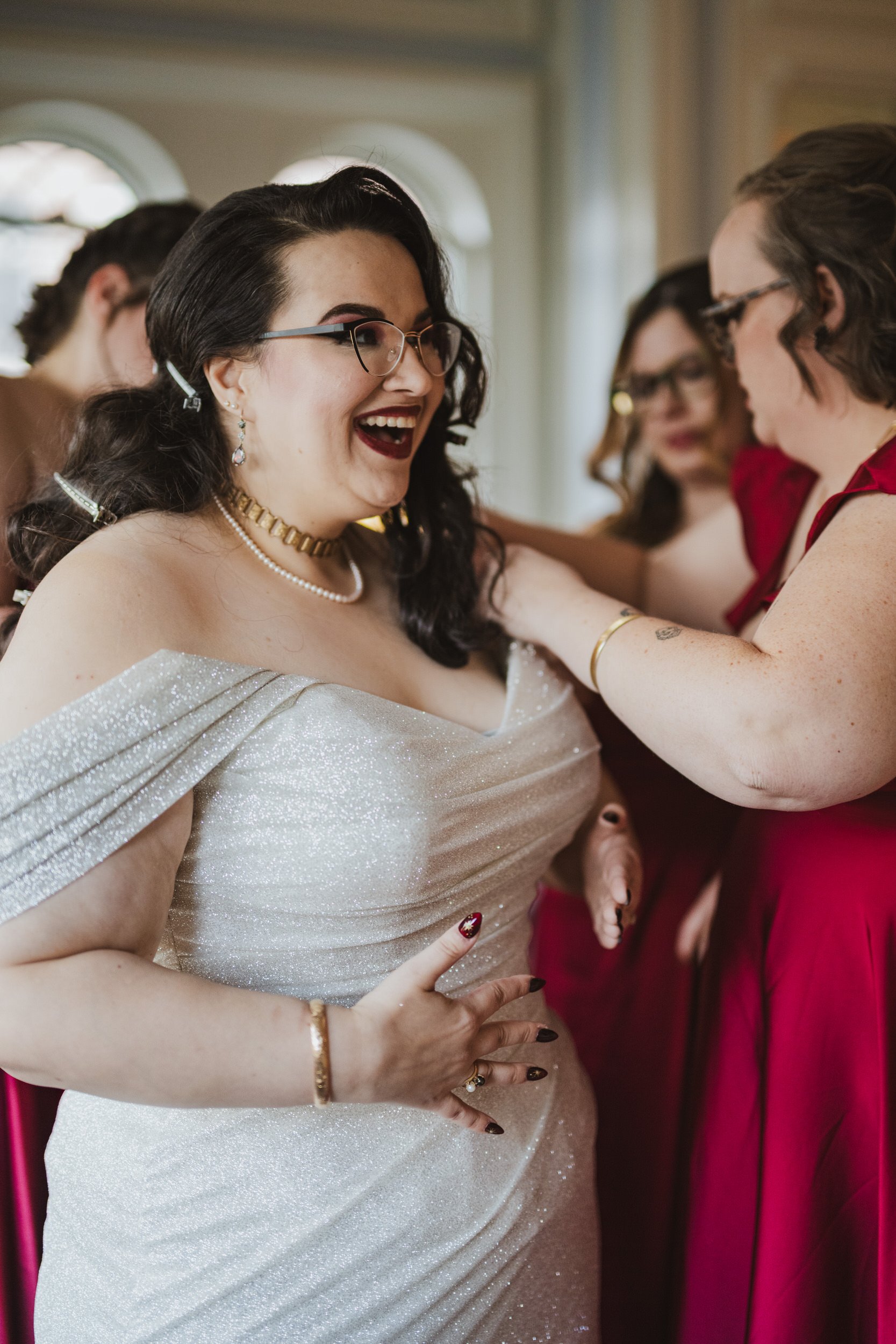A person smiling as someone helps them adjust their wedding dress