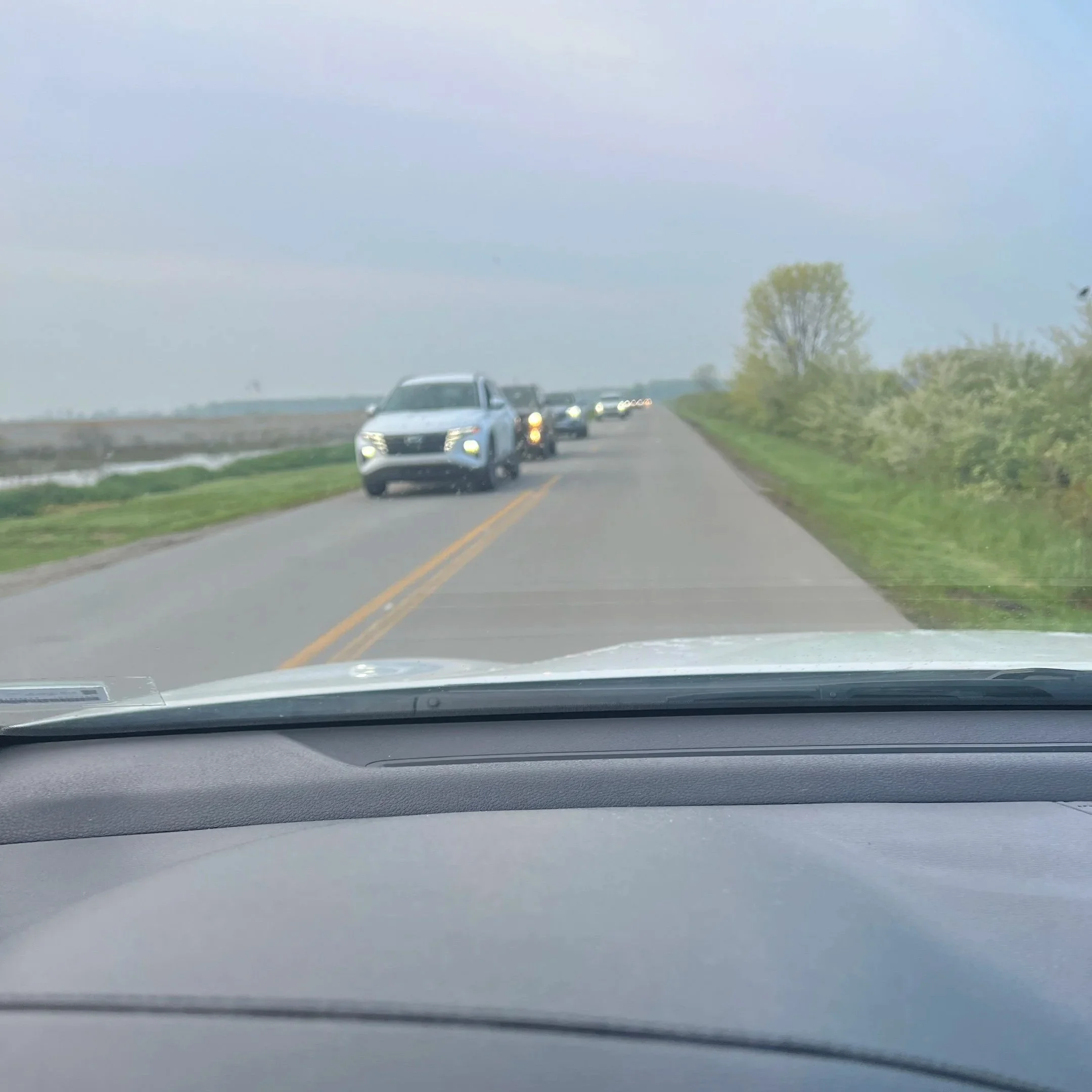 View of approaching cars seen through the dashboard windshield of a car. Approaching cars are in a long line with headlights on.