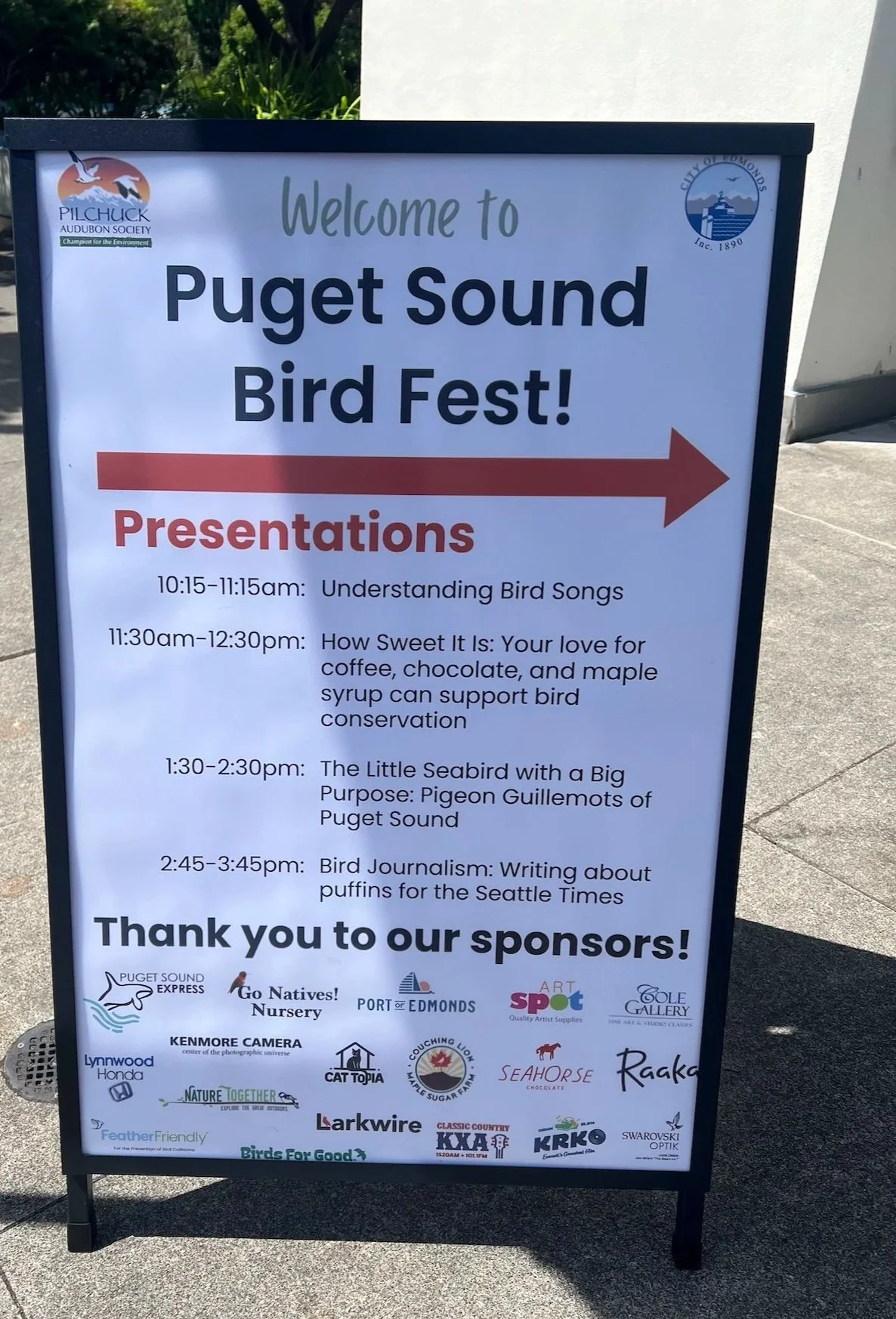 A sign displaying the list of speaking topics for the afternoon of the Puget Sound Bird Fest, with a directional arrow indicating location of the speaker venue.