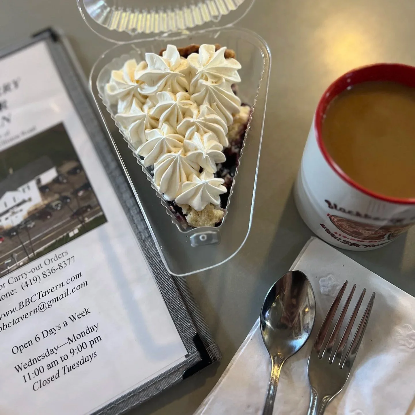 Slice of whipped cream covered berry pie next to a cup of coffee and menu for Blackberry Corners Tavern