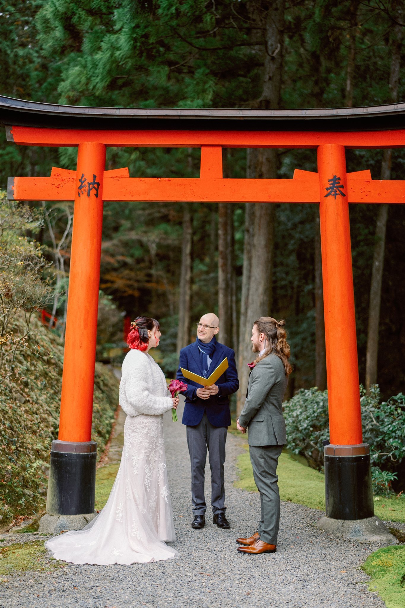 Couple stand in front of red Tori gate at their Japan elopement ceremony. 