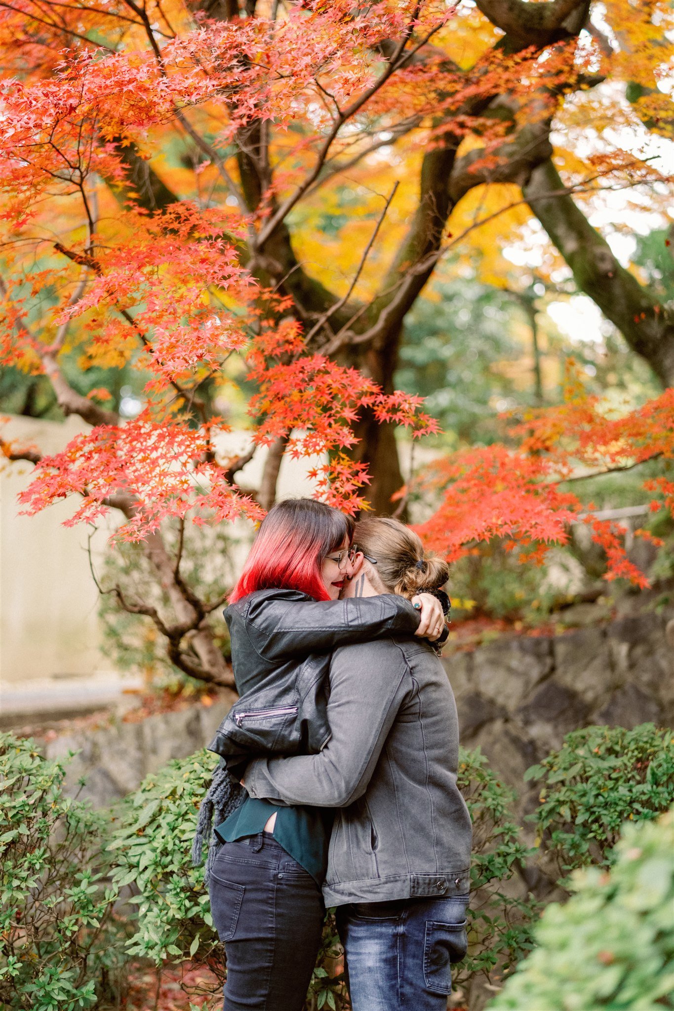 Couple embrace during their engagement session in front of vibrant red and yellow autumn foliage. 