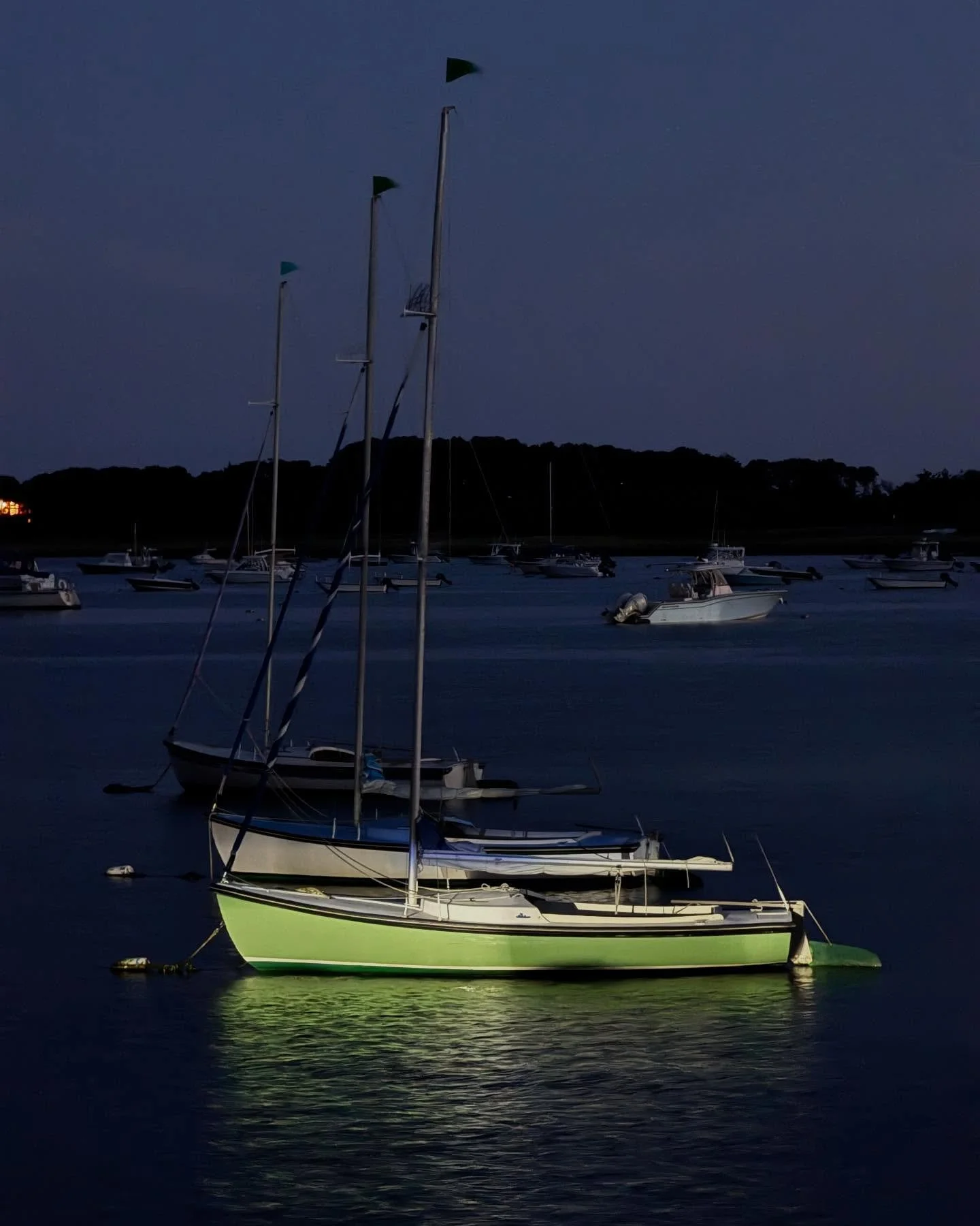 Headlights on the wharf illuminate the sailboats.