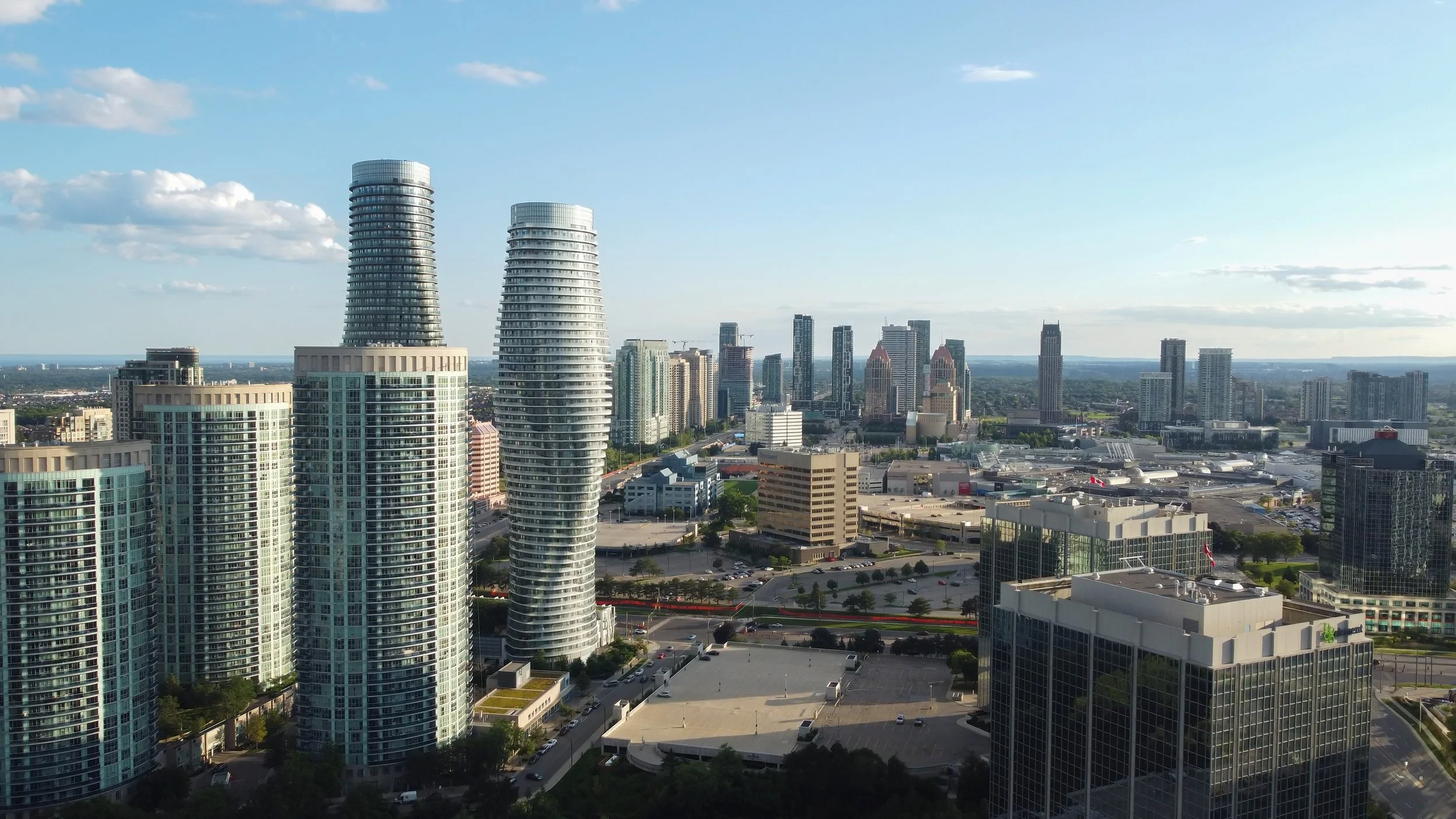 Skyscrapers and high-rise buildings in a city skyline during daytime, with a partly cloudy sky and distant horizon.
