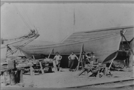 Four men in front of wooden boat Menotti Pasquinucci, an Italian immigrant, (holding hand saw) with newly built vessel and boatwrights, circa 1907.