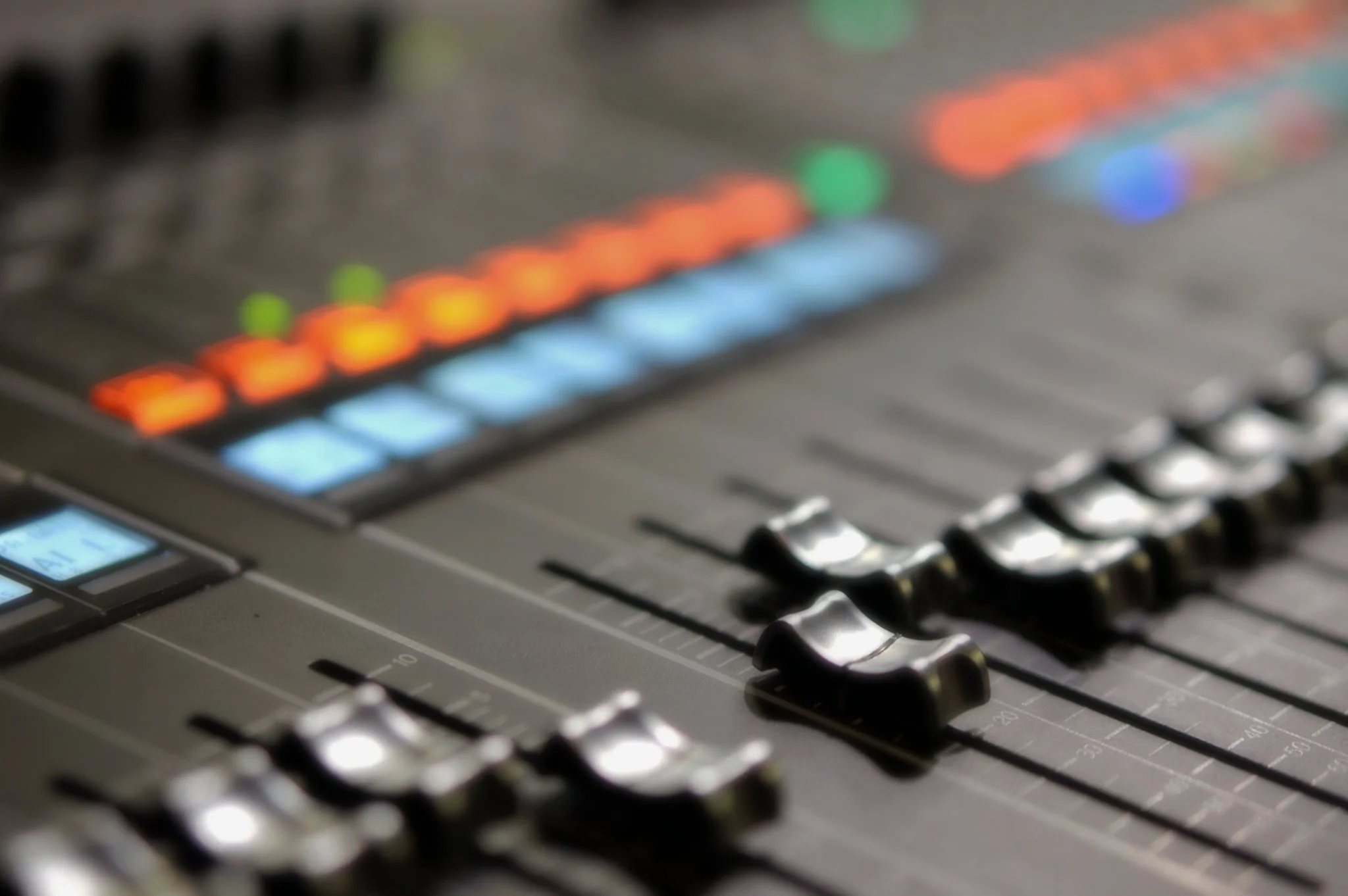Close-up of an audio mixing console with faders and illuminated buttons.