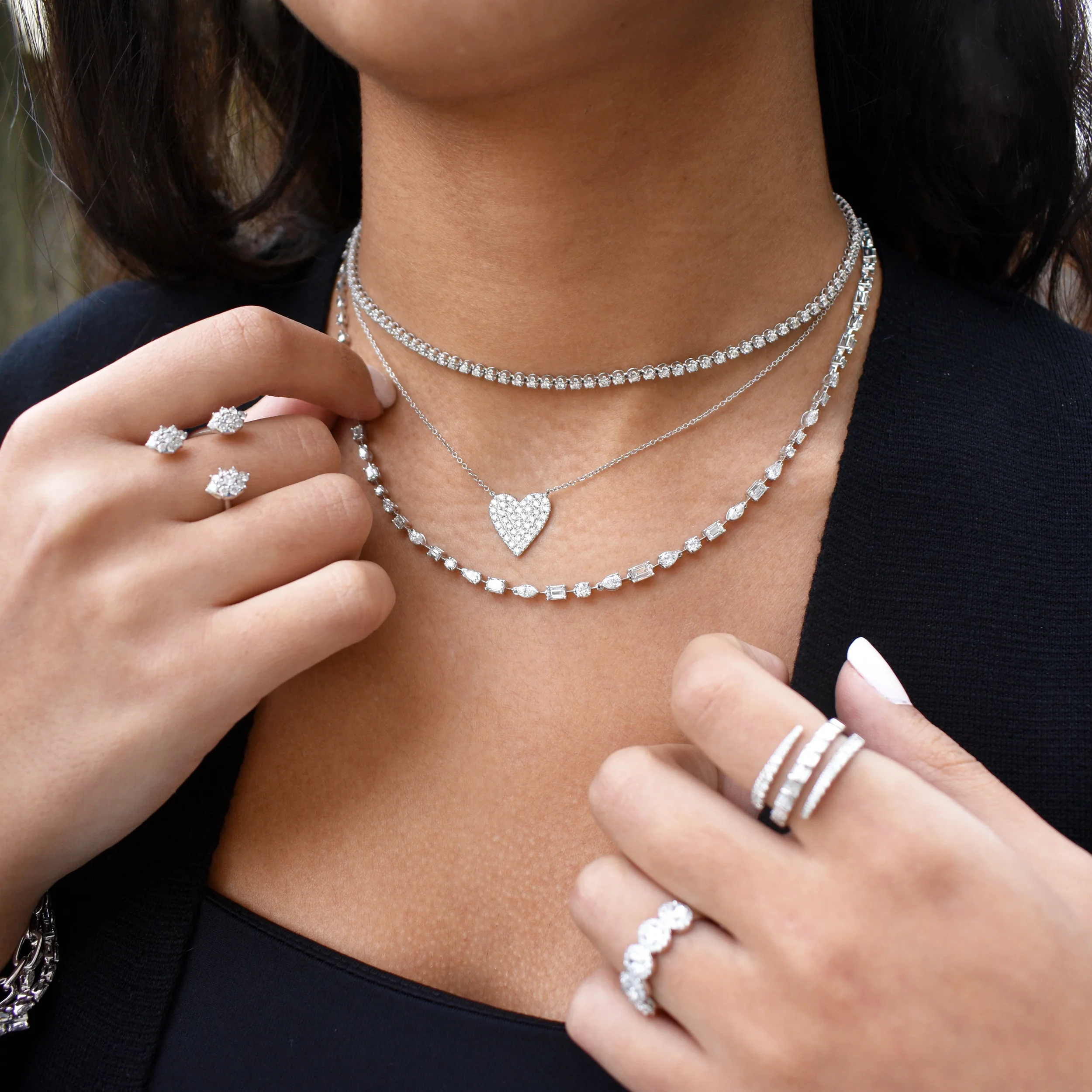 Diamond heart necklace layered with tennis necklaces and diamond rings. (Copy)