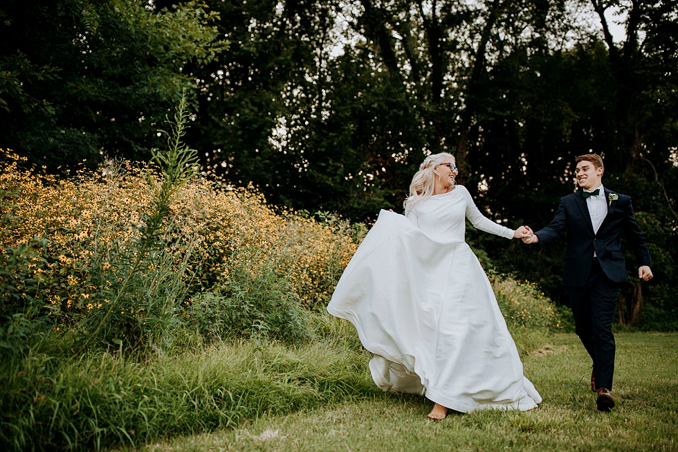  hand in hand bride and groom run through the natural greenery wedding reception venue #weddingphotographer #broaduschapel #weddingdaybliss #louisvillephotographer #kentuckyweddingphotographer #weddingsession #photographyanddesignbylauren #weddingcer