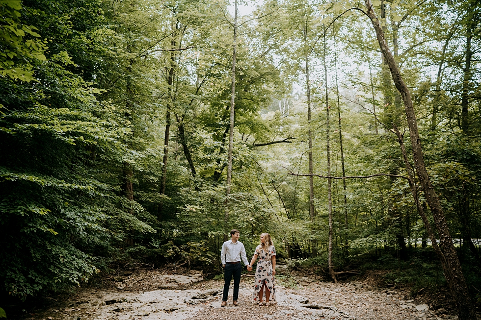  Middle of the forest photo of engaged couple holding hands with sun shining through the forest trees #engagementphotographer #bernheimforest #engagementgoals #kentuckyengagementphotographer #kentuckyphotographer #engagementsession #photographyanddes