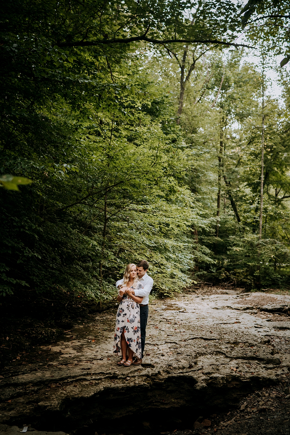  Groom to be embraces bride to be in the middle of the forest floral dress and sun through the trees #engagementphotographer #bernheimforest #engagementgoals #kentuckyengagementphotographer #kentuckyphotographer #engagementsession #photographyanddesi