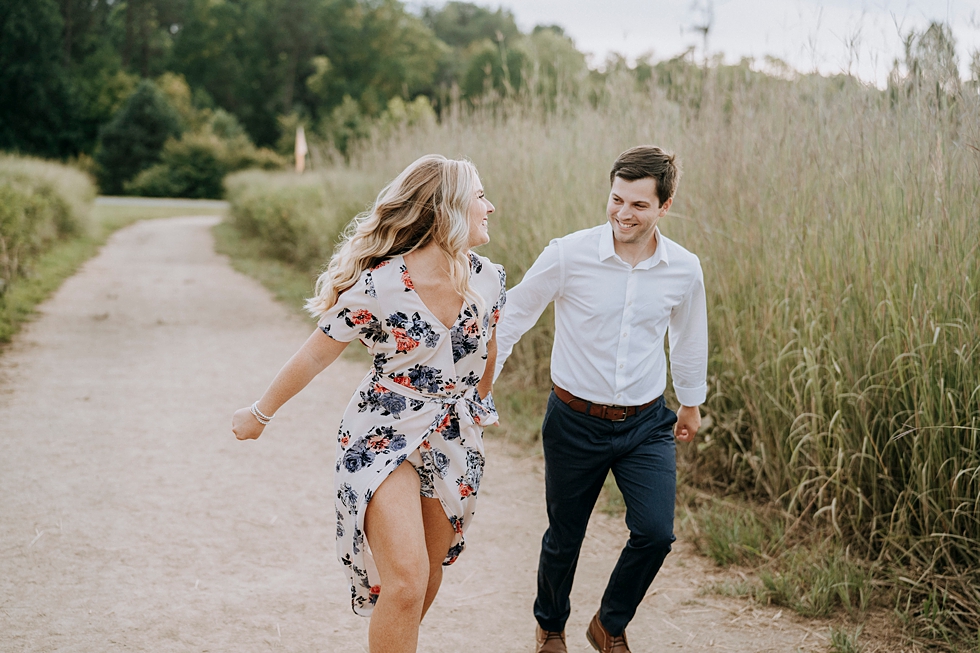  Engaged couple running together on forest path in semi formal attire #engagementphotographer #bernheimforest #engagementgoals #kentuckyengagementphotographer #kentuckyphotographer #engagementsession #photographyanddesignbylauren 