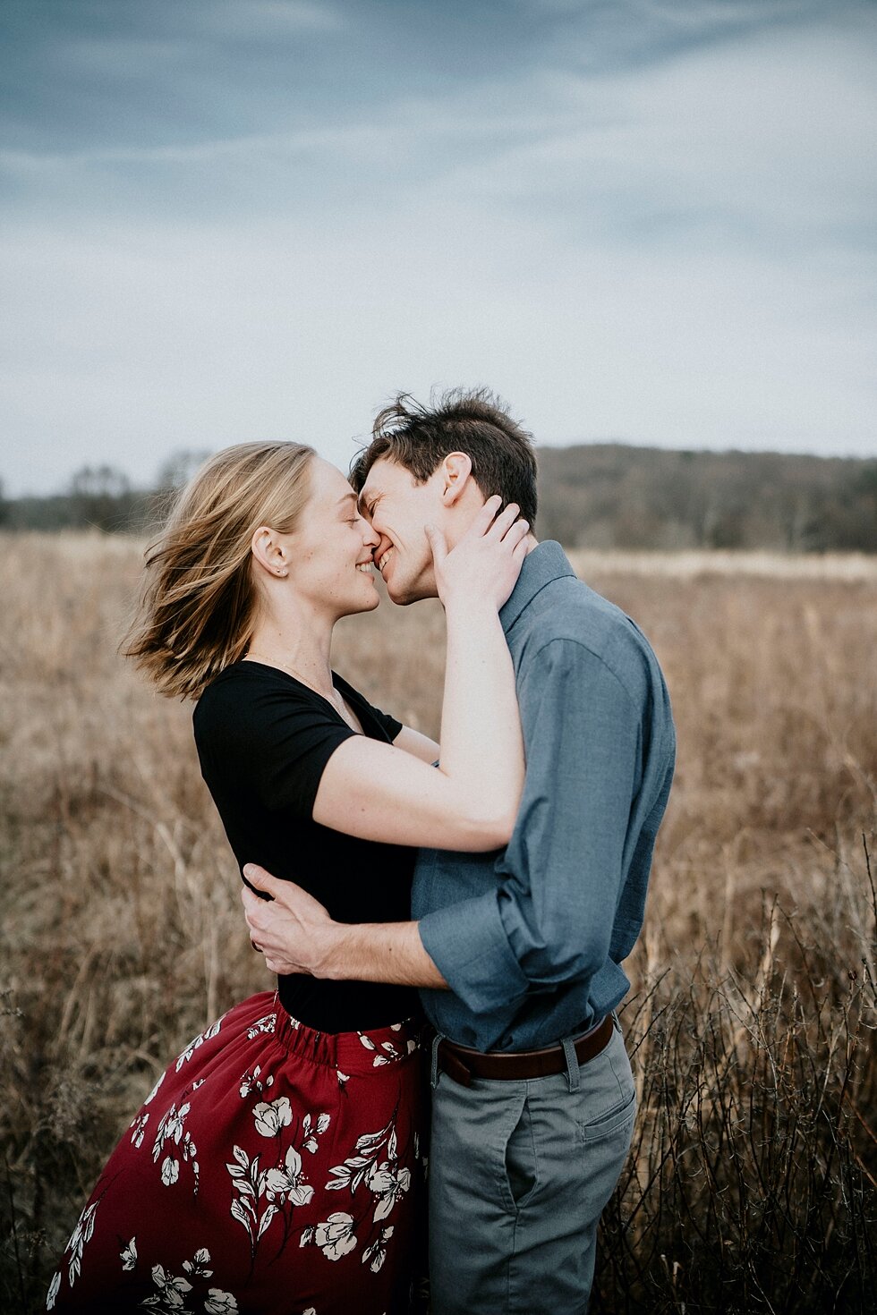 Head over heals couple sharing a kiss in the Kentucky outdoors for their engagement session in Louiseville, Kentucky. Kentucky mountains red floral skirt dark black shirt cloudy skies engagement session Photography by Lauren outdoor #photographybyla