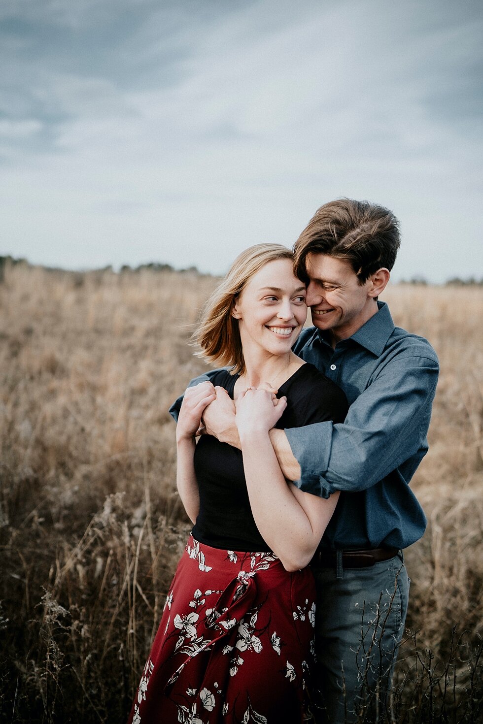  Smiles that were contagious from this couple as they celebrated their engagement and shared their plans of getting married. Kentucky mountains red floral skirt dark black shirt cloudy skies engagement session Photography by Lauren outdoor #photograp