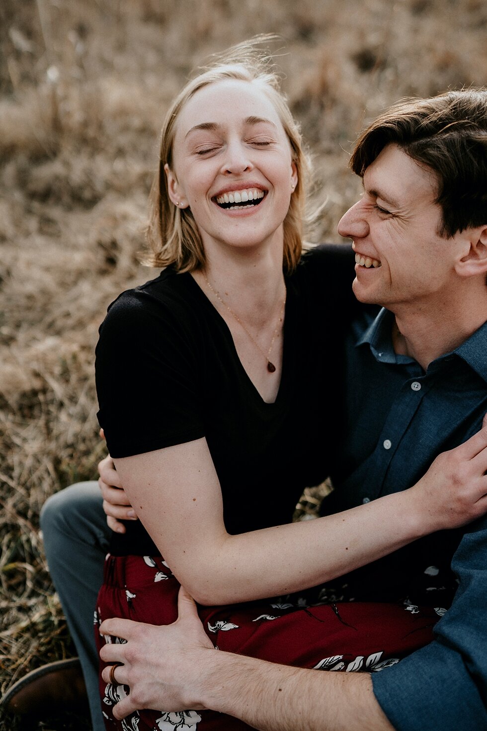  There is nothing like a good laugh shared between two people in love. Kentucky mountains red floral skirt dark black shirt cloudy skies engagement session Photography by Lauren outdoor #photographybylauren #kentuckyengagementphotography #bernheimfor