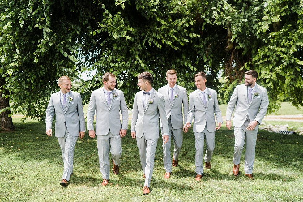 Groom and groomsmen walking together on wedding day with greenery in the background making their grey suits stand out against the bright background. #thatsdarling #weddingday #weddinginspiration #weddingphoto #love #justmarried #midwestphotographer 