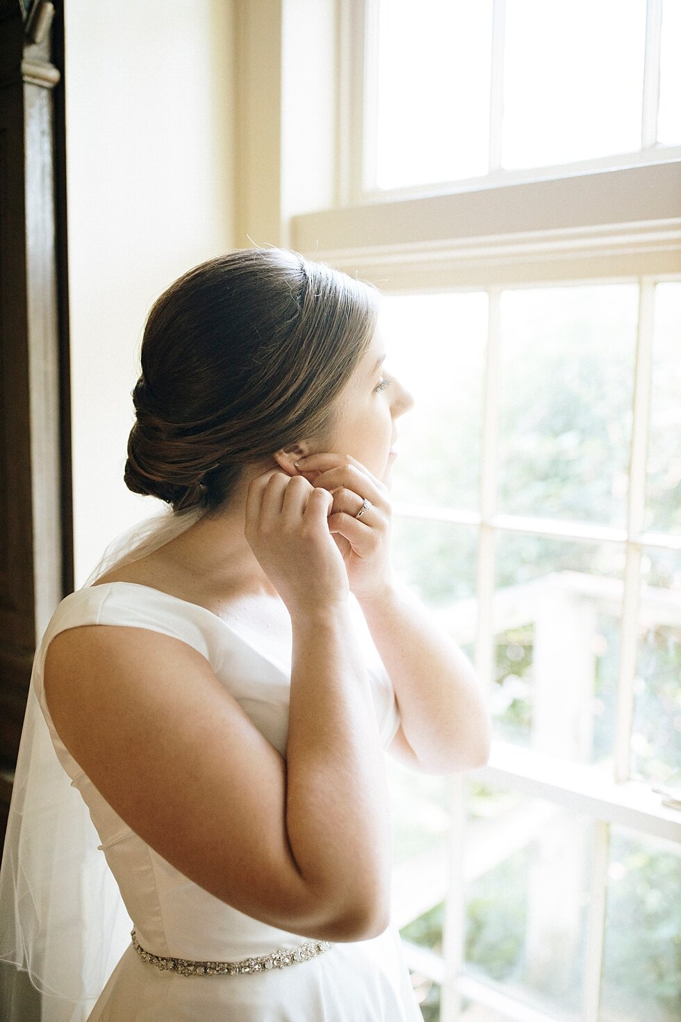  bride getting ready and putting on earrings facing out window  #thatsdarling #weddingday #weddinginspiration #weddingphoto #love #justmarried #midwestphotographer #kywedding #louisville #kentuckywedding #louisvillekyweddingphotographer #weddingbliss