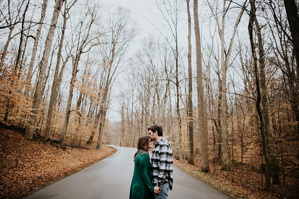  Kiss on the forehead between engaged couple at Bernheim Forest in Louisville, Kentucky. Louisville photographer winter engagement Bernheim Forest emerald green dress plaid shirt rainy day Kentucky couple outdoor engagement  #savethedates #engagement