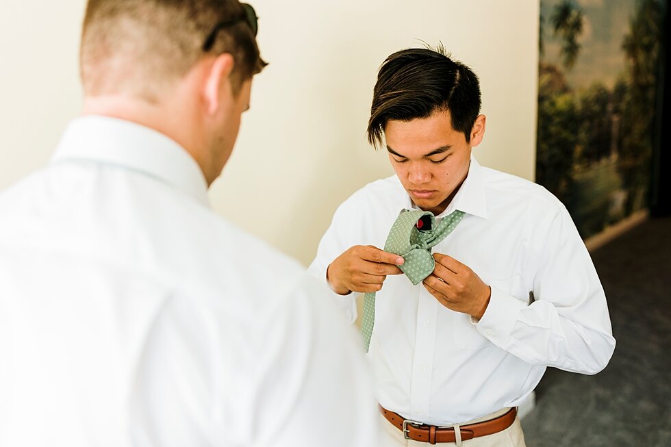  The groom getting the final touches ready on his wardrobe before meeting his future wife at the end of the aisle. Romantic casual lace wedding gown close friends neutral colors background wedding natural greenery crisp white #midwestphotographer #ky