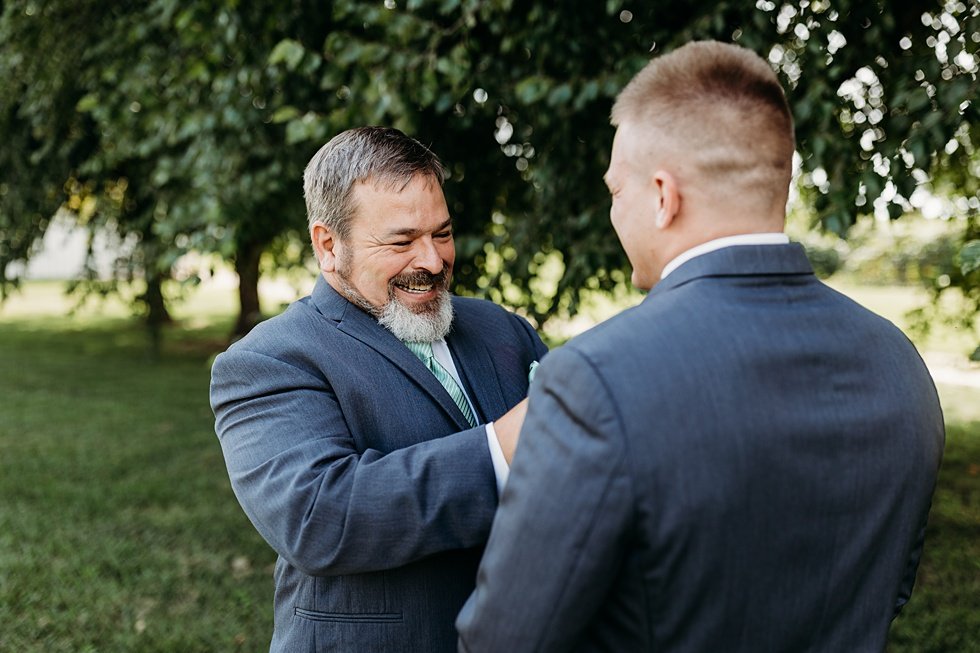  Groom's father pinning on boutonniere. Outdoor summer wedding at Huber's Orchard and Winery in Starlight, Indiana. 