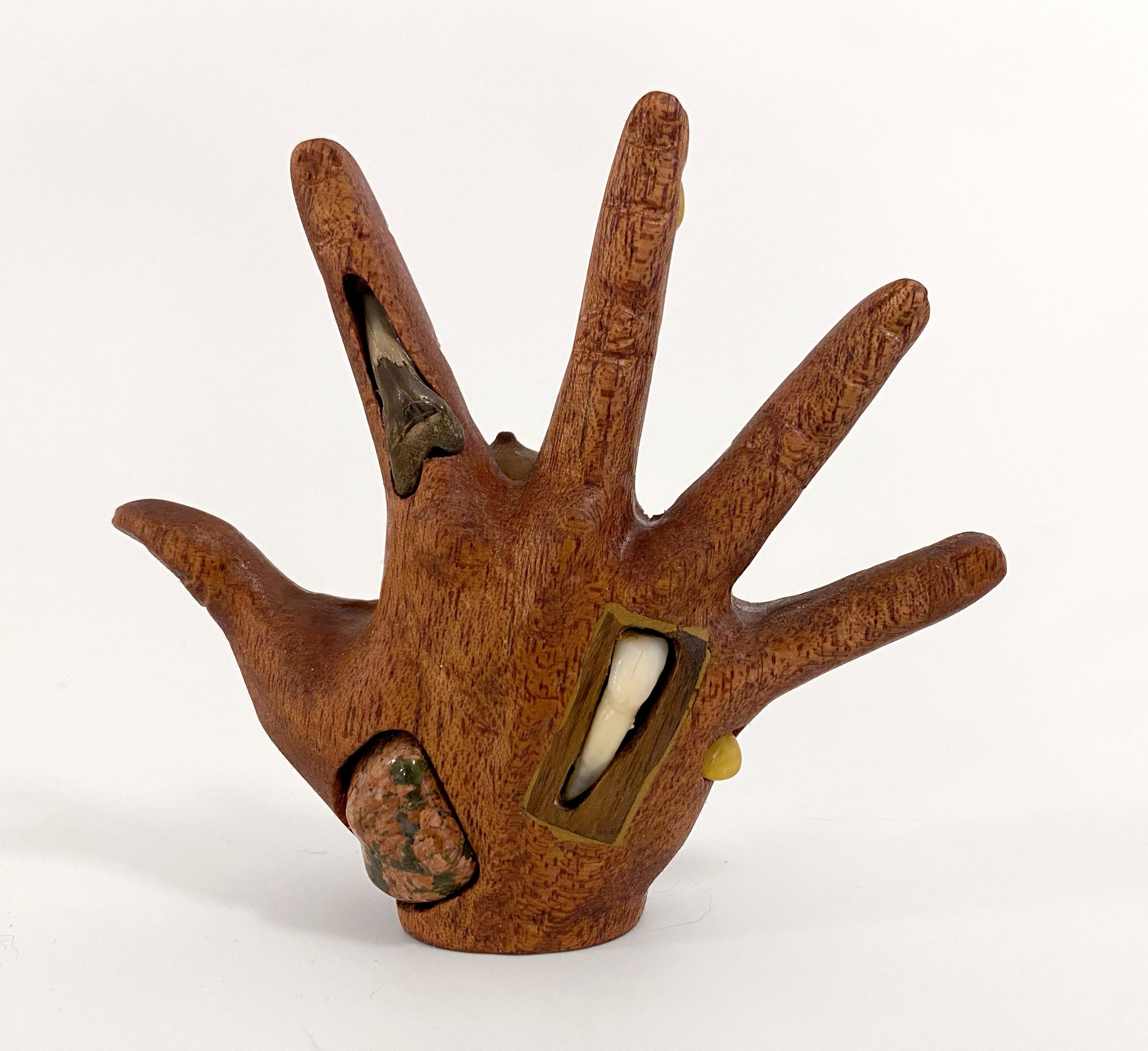   Hand with Tooth , 2023, human tooth, acorn, rocks, amber, fossil, bead, and walnut on carved mahogany, 4.5” x 4.5” x 1.5” 