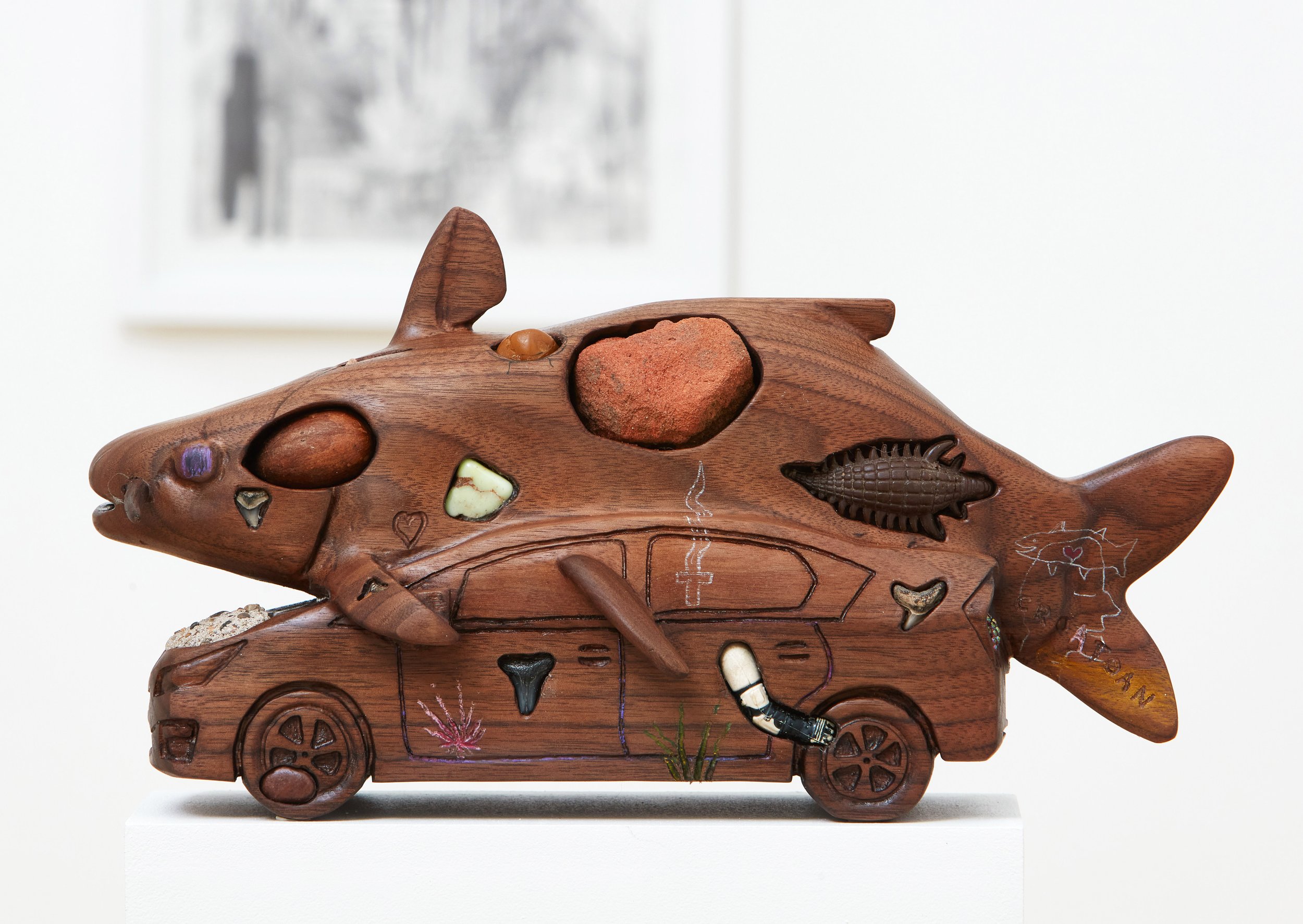  Catfish/Prius , 2022, meteorite, fossils, rocks, amber, brick, concrete, porcelain, aluminum, iron, plastic toys, and colored pencil on carved walnut, 13” x 8” x 6” 