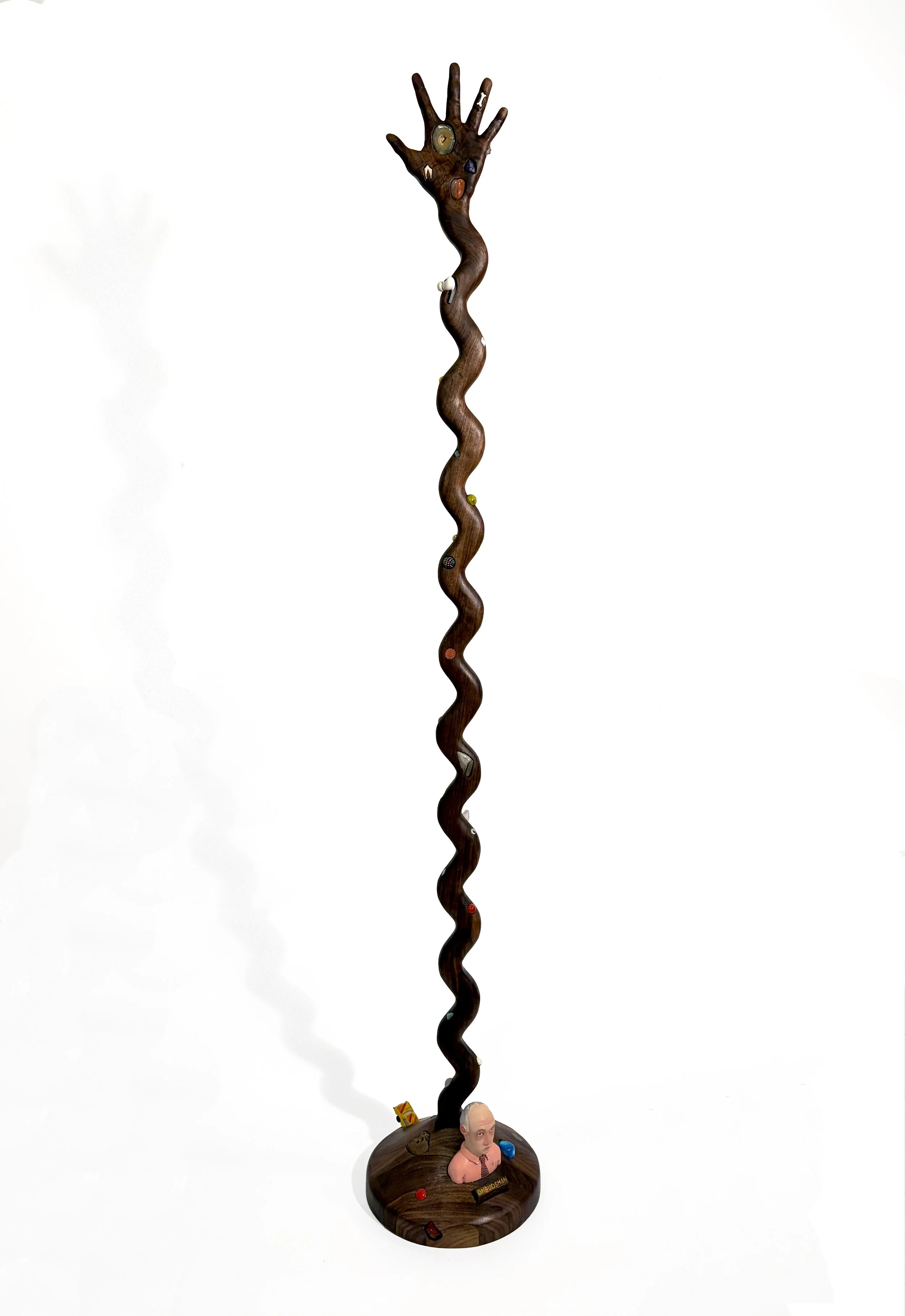   Hand Stand , 2026, meteorite, coyote tooth, Apple AirPod, toy car, rocks, Legos, fossils, turquoise, broken dice, beads, steel penny, buttons, mosaic tile, marbles, and oil paint on carved walnut, 58“ x 9.5” diameter 